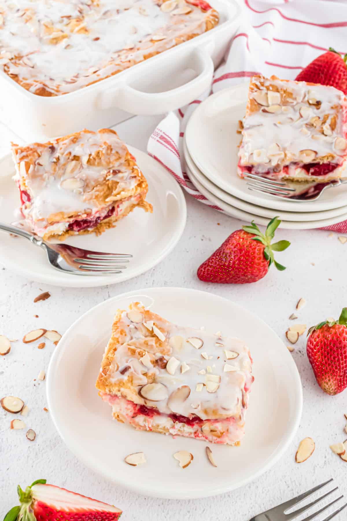 Slices of strawberry cream cheese bars on white plates.