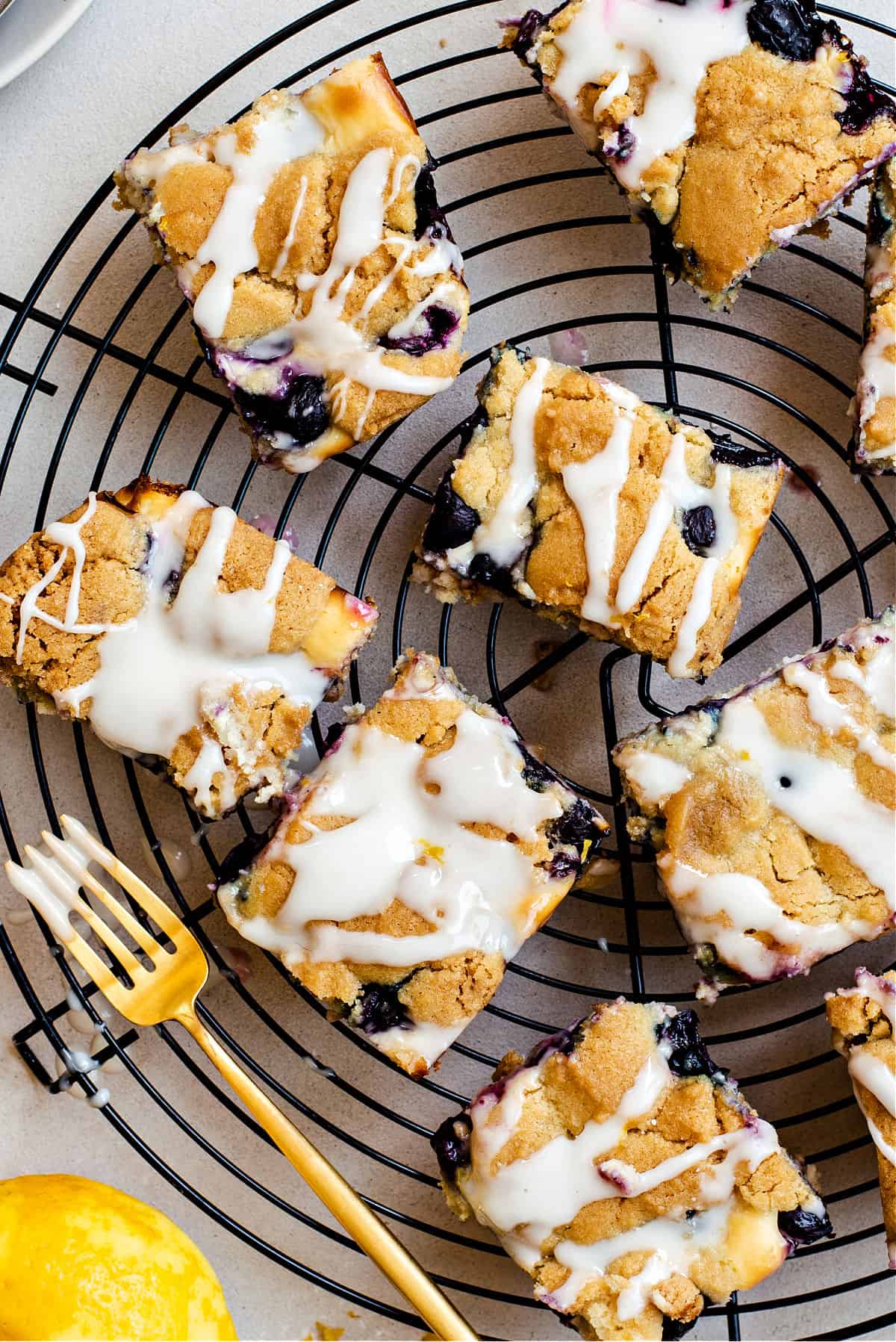Blueberry cheesecake bars on a wire rack with a lemon glaze on top.