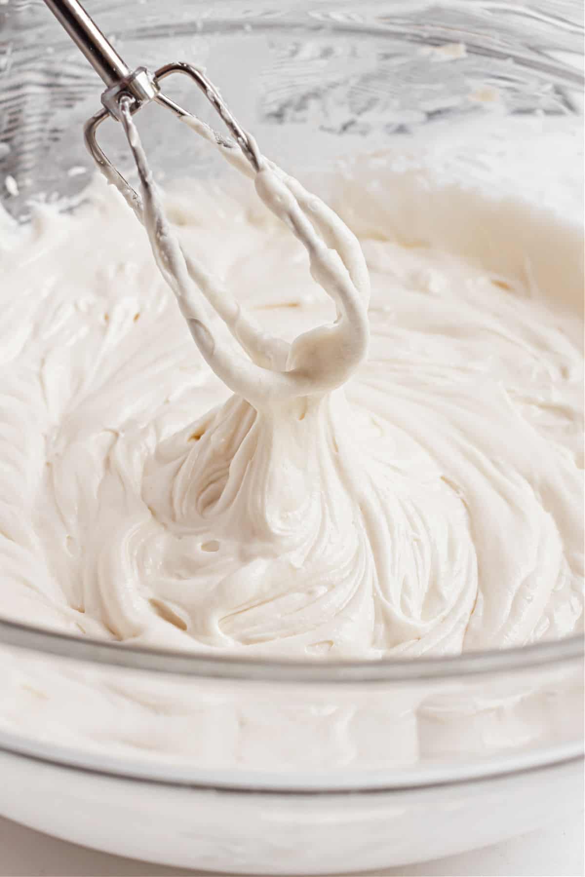 Vanilla frosting made with sour cream in a clear glass mixing bowl.