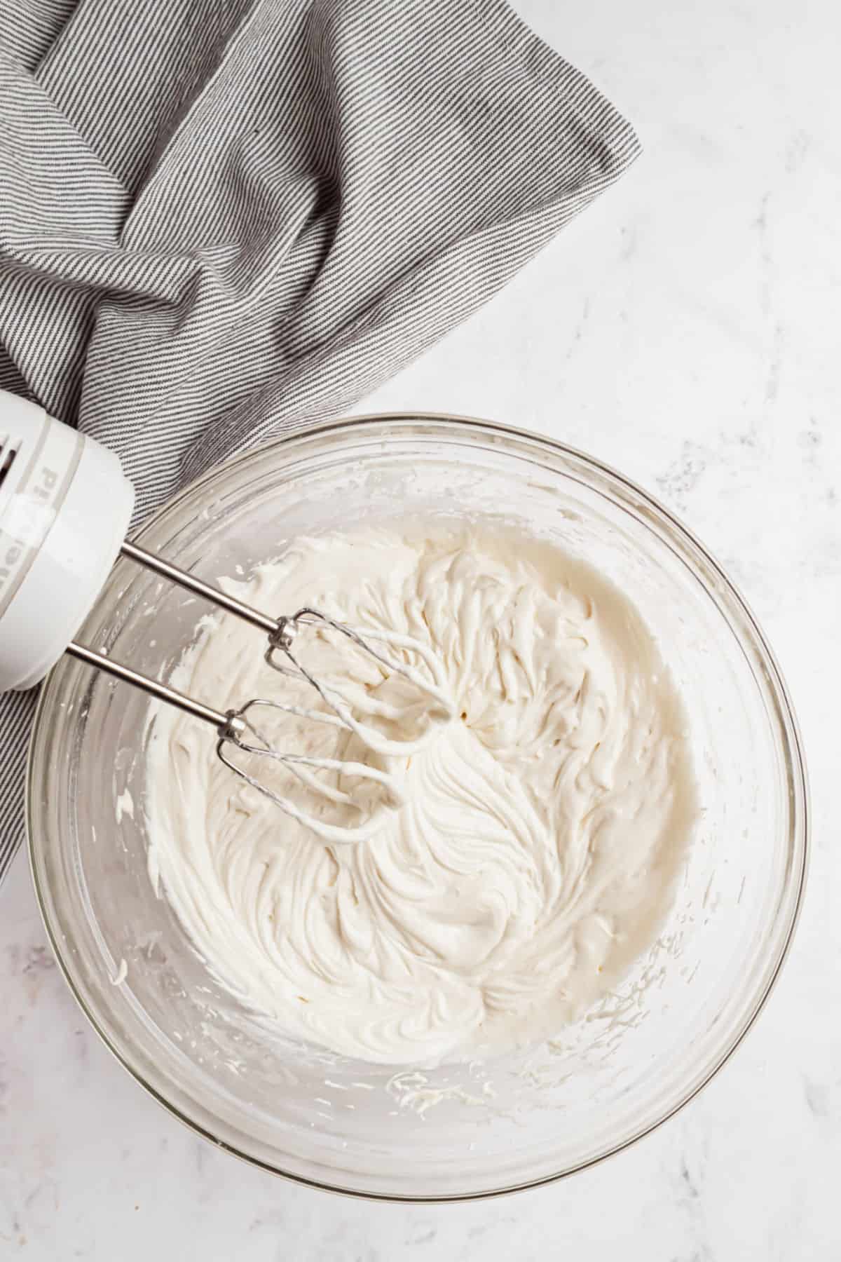 Sour cream frosting in mixing bowl with hand mixer.