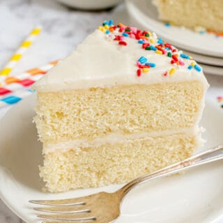 Slice of vanilla layer cake with vanilla sour cream frosting on white plate.