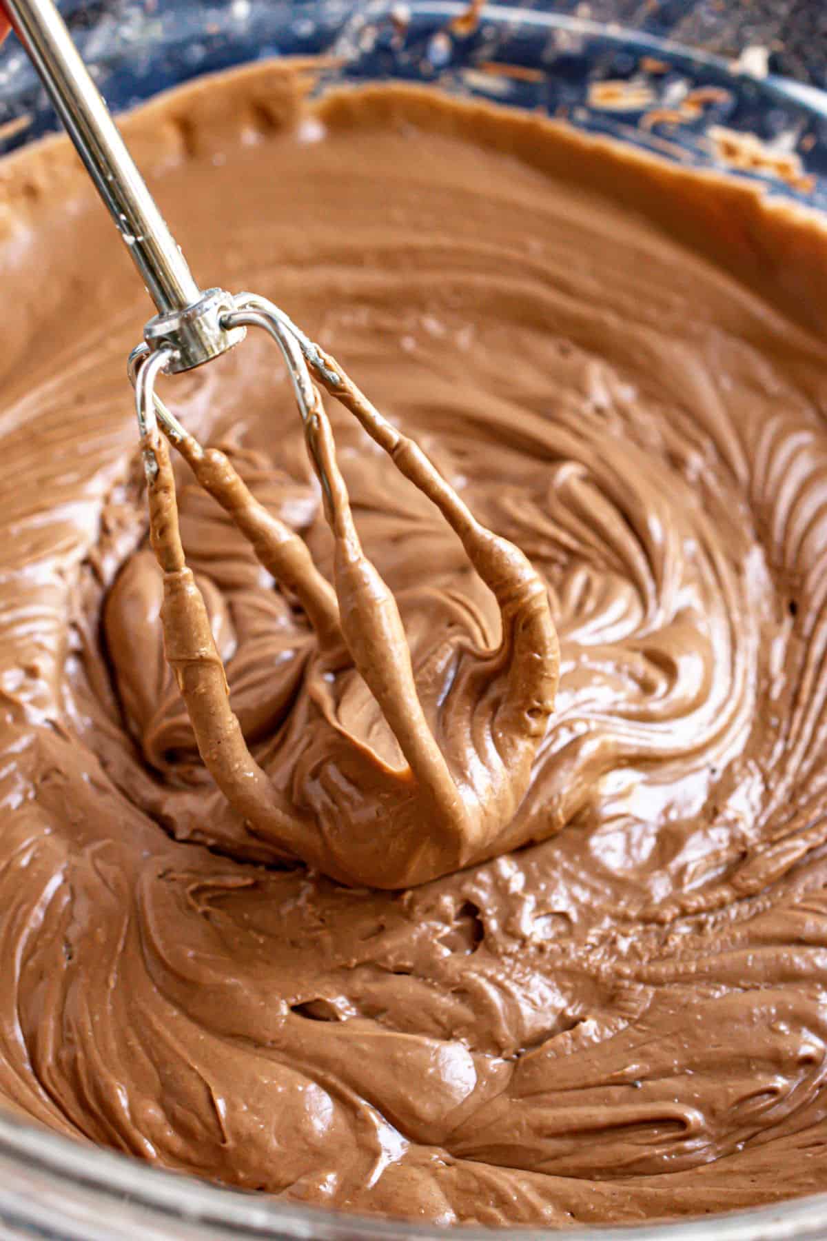 Smooth and creamy chocolate frosting in a glass bowl with a beater.