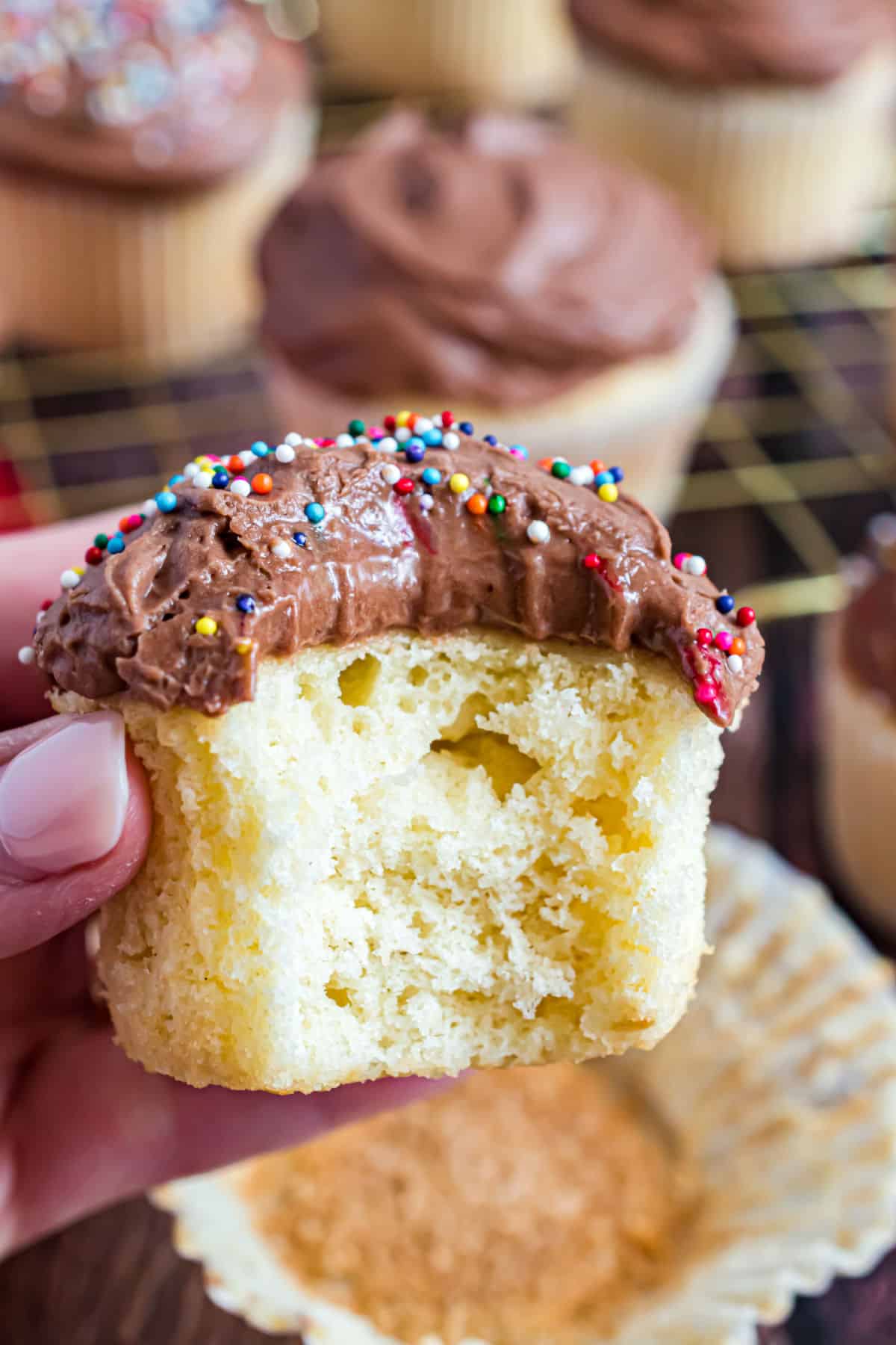 Chocolate frosting on yellow cupcake and one bite removed.