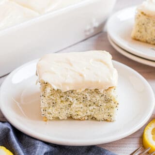 Slice of lemon poppy seed cake with lemon cream cheese frosting on a white plate.