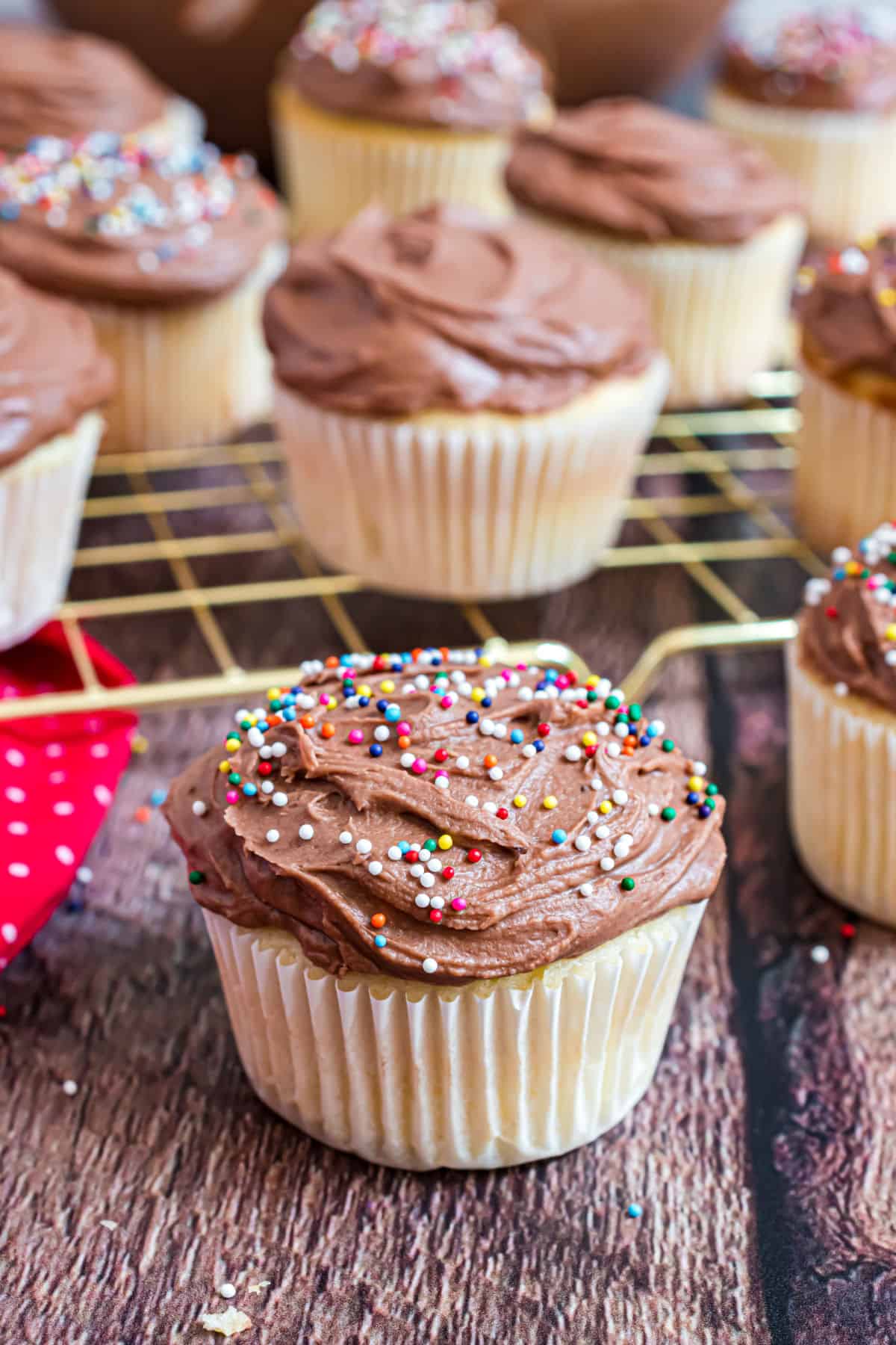 Yellow cupcakes on wire cooling rack with chocolate frosting and sprinkles.