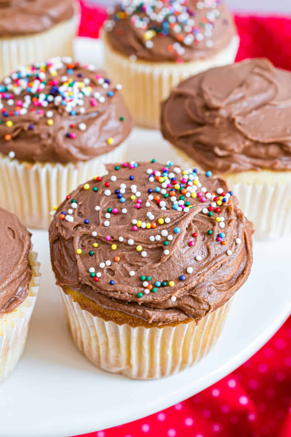 Yellow cupcakes with chocolate frosting served on white cake platter.