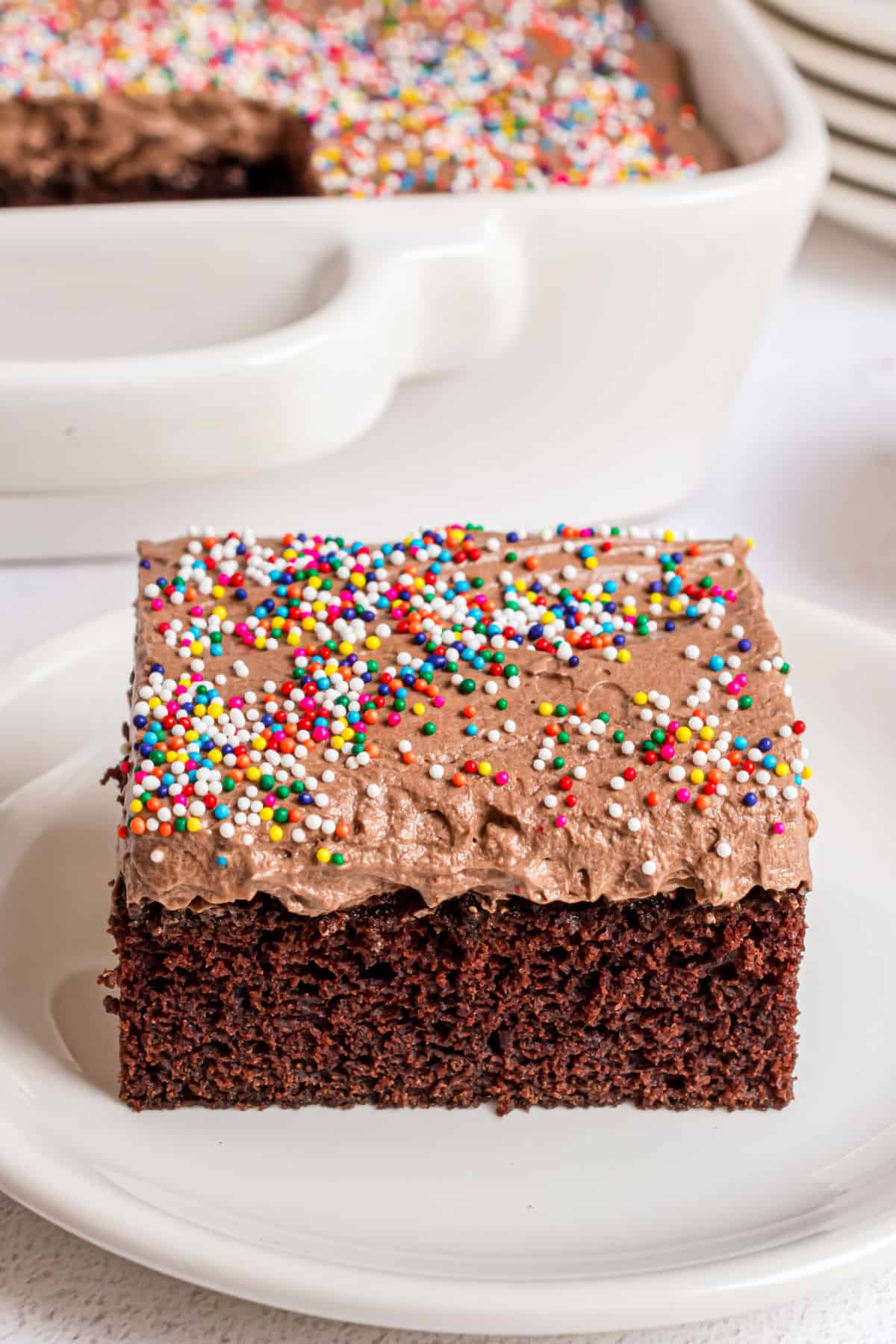 Easy chocolate cake slice on a white plate with sprinkles.