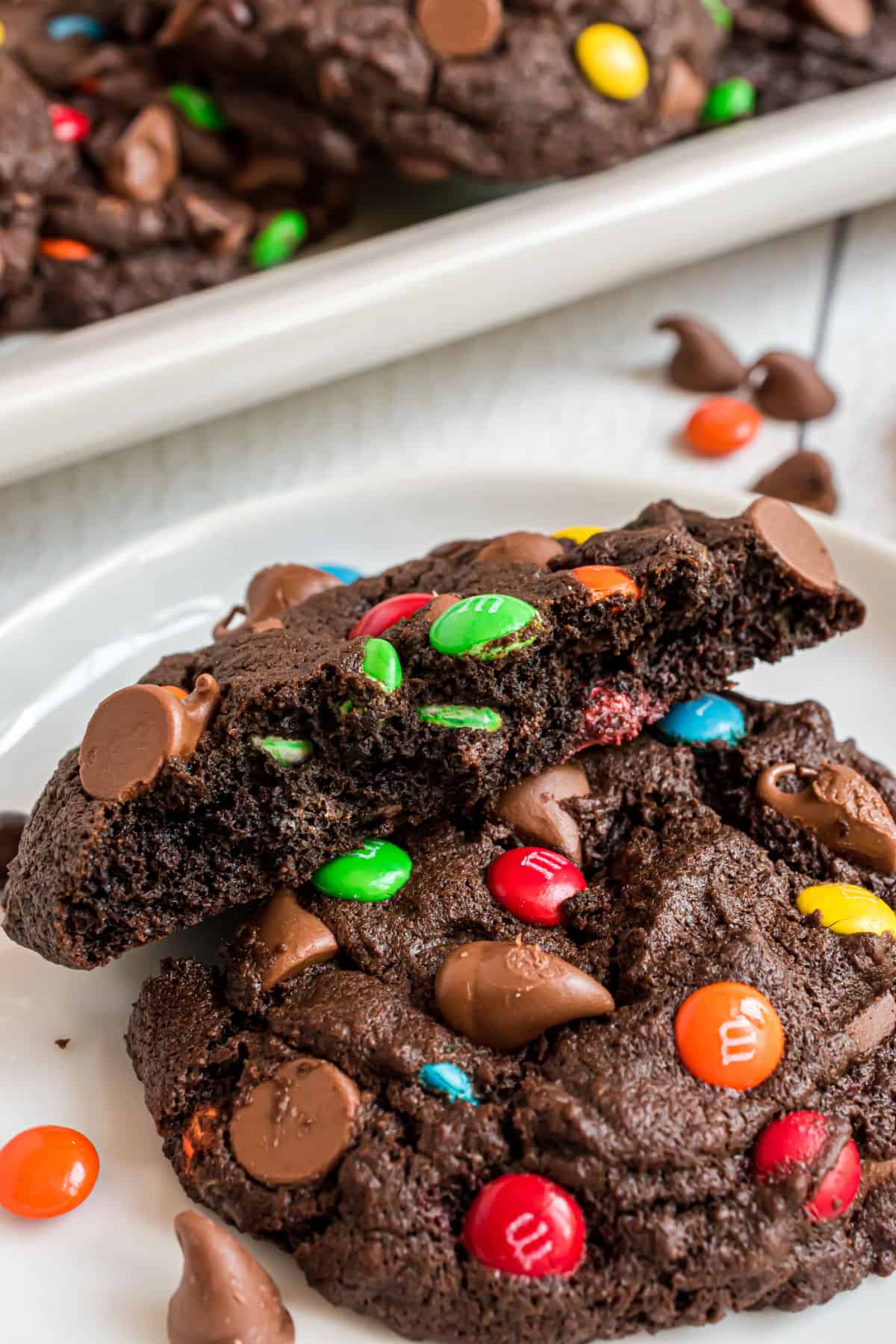 Two chocolate M&M cookies on a white plate, one broken in half.