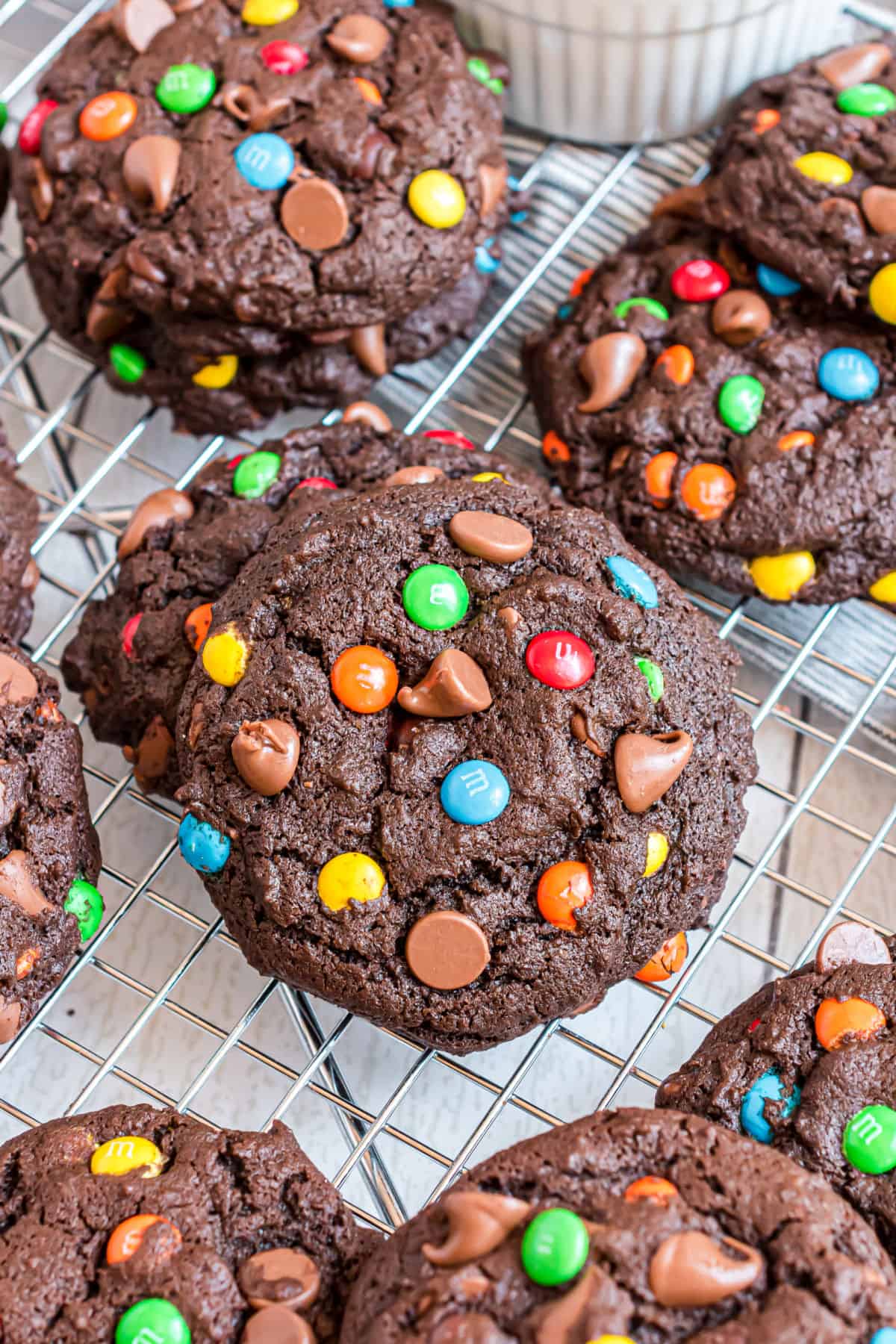 Stacks of chocolate cookies with M&M's on wire cooling rack.