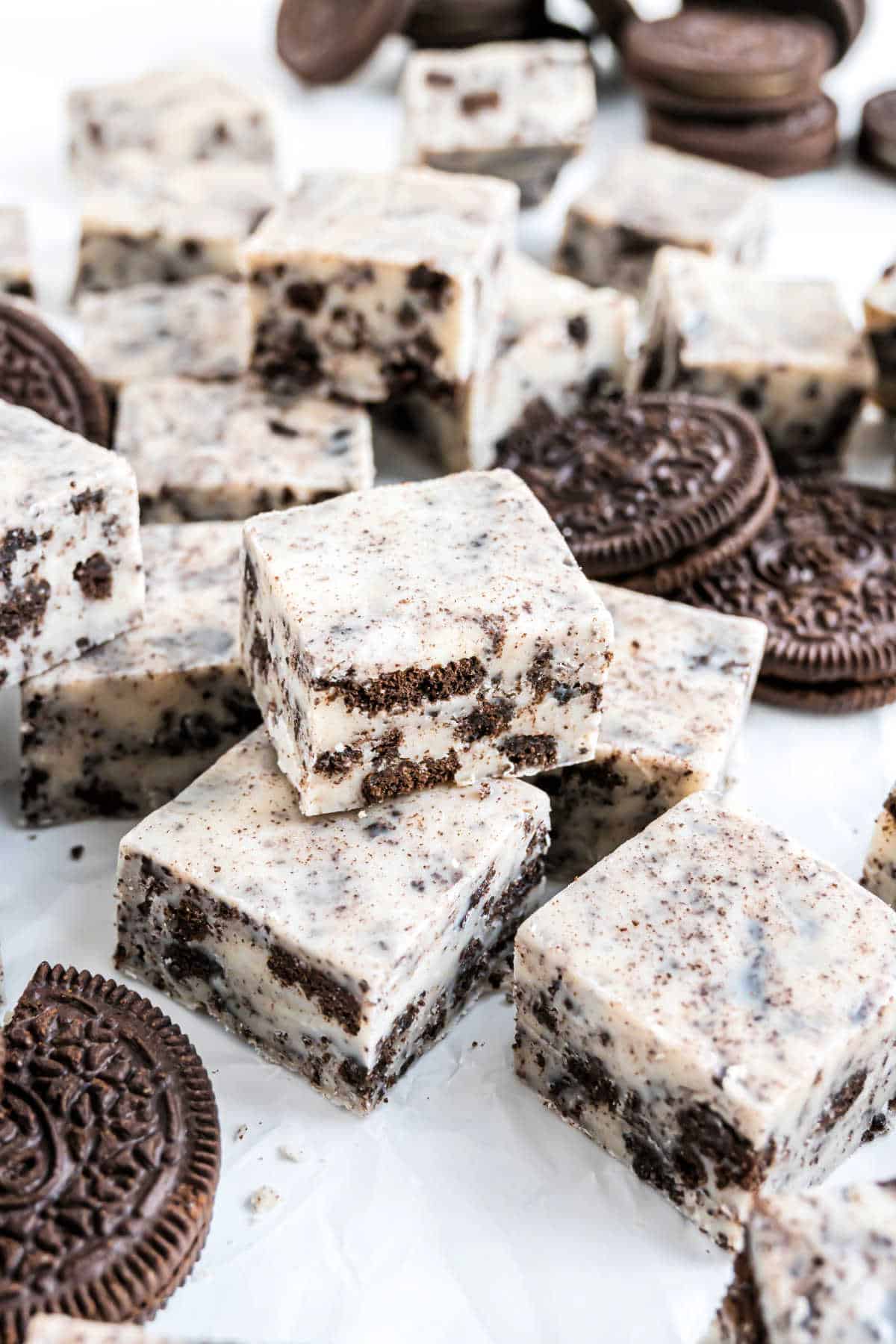 Squares of cookies and cream fudge are surrounded by chocolate sandwich cookies on a white surface, highlighting the creamy texture and rich flavor of this classic cookies and cream fudge treat.