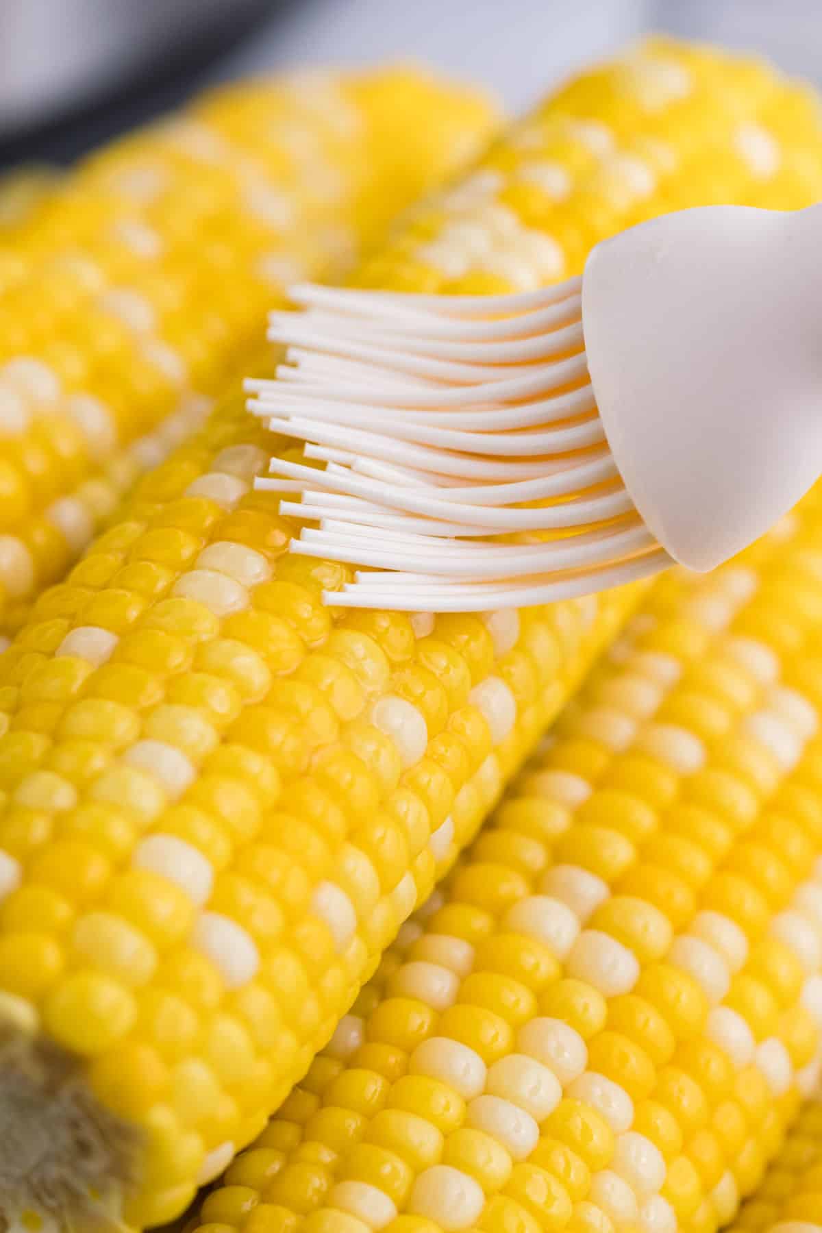 Corn on the cob brushed with melted butter using a pastry brush.