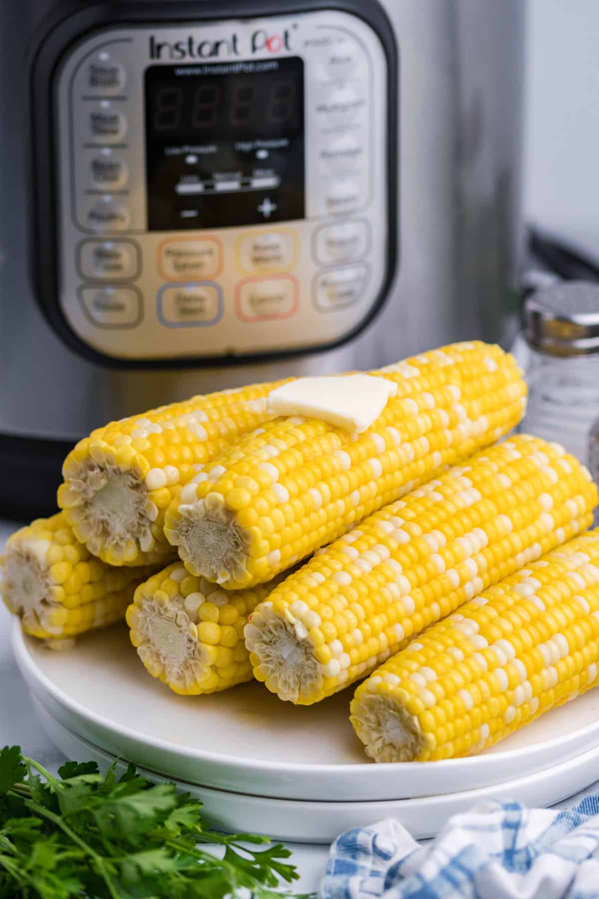 Corn on the cob stacked on a plate with instant pot in background.