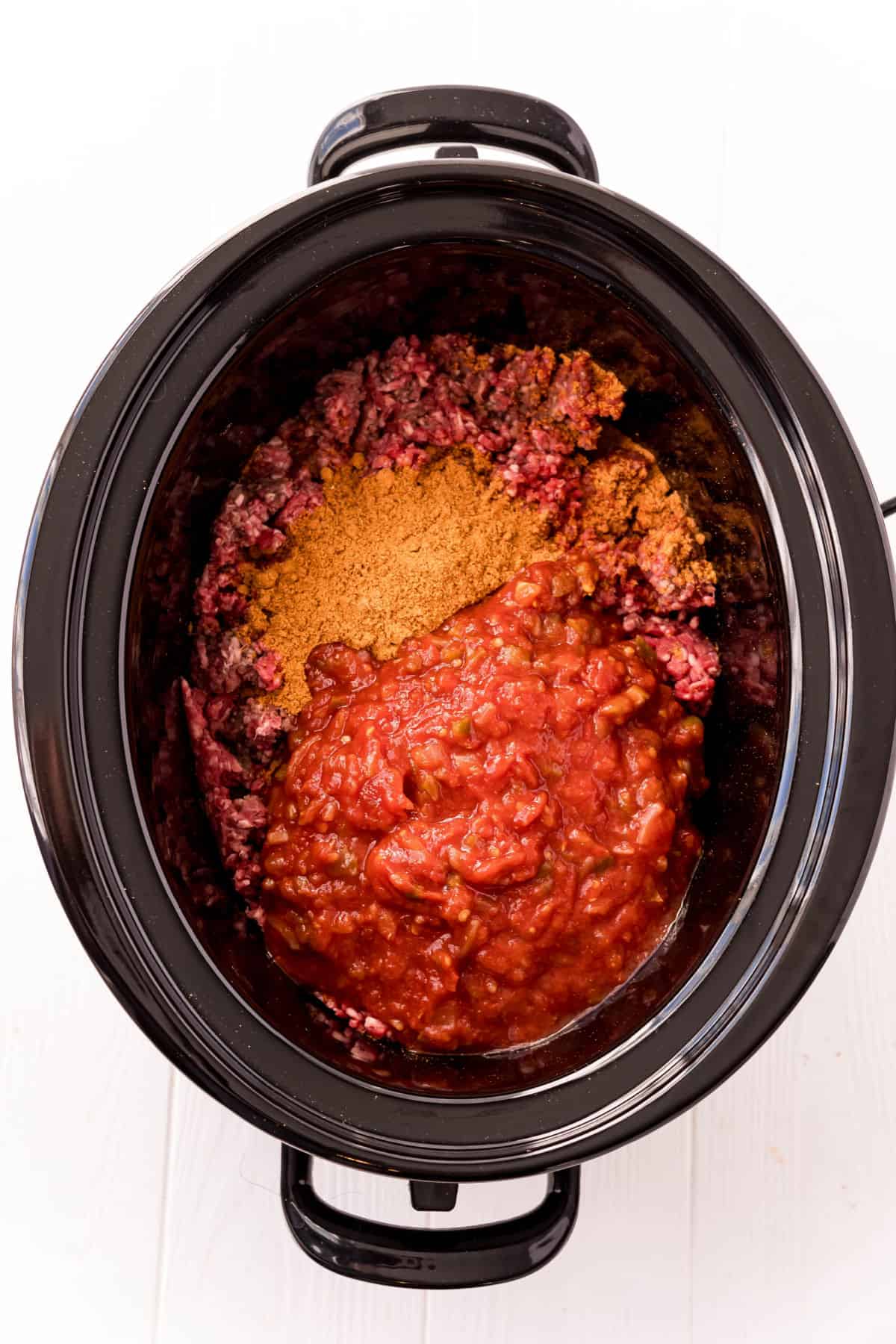 Black slow cooker with ingredients to make taco meat inside.