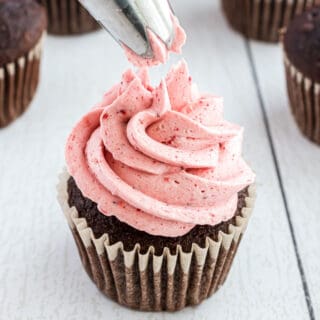 Strawberry frosting being piped onto a chocolate cupcake.