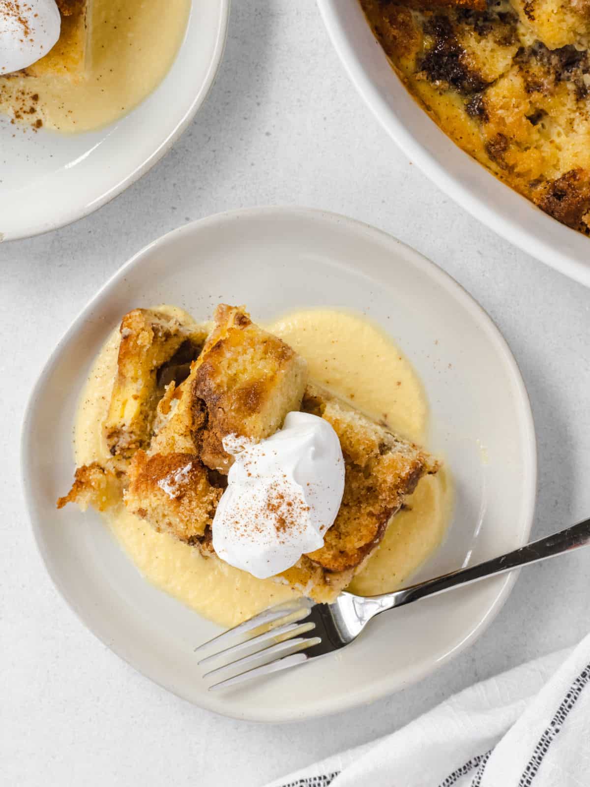 Apple bread pudding served with vanilla creme anglaise onn a white dessert plate.