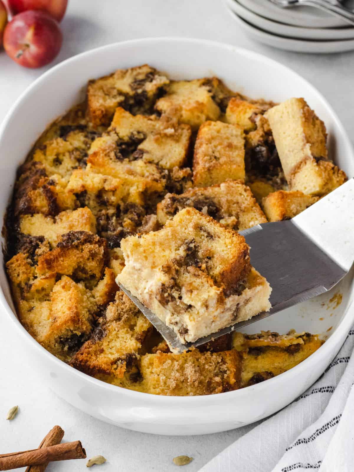 Apple bread pudding baked in an oval casserole with one slice removed on spatula.
