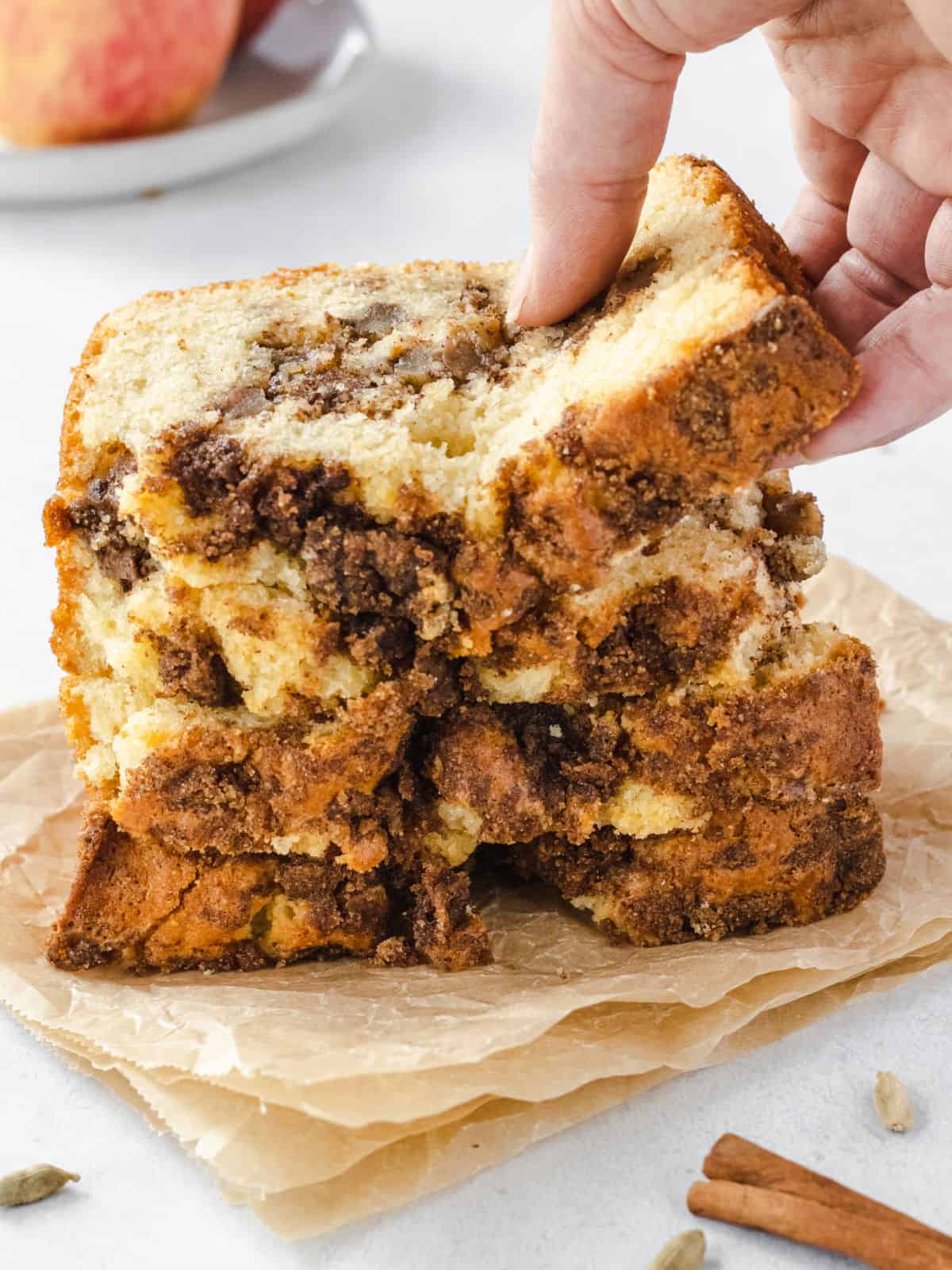 Slices of chai apple bread stacked on parchment paper with one slice being lifted up.