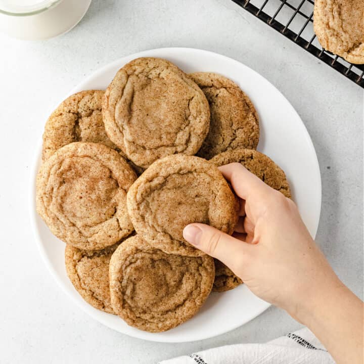 White plate with stack of chai cookies and a hand taking one away.