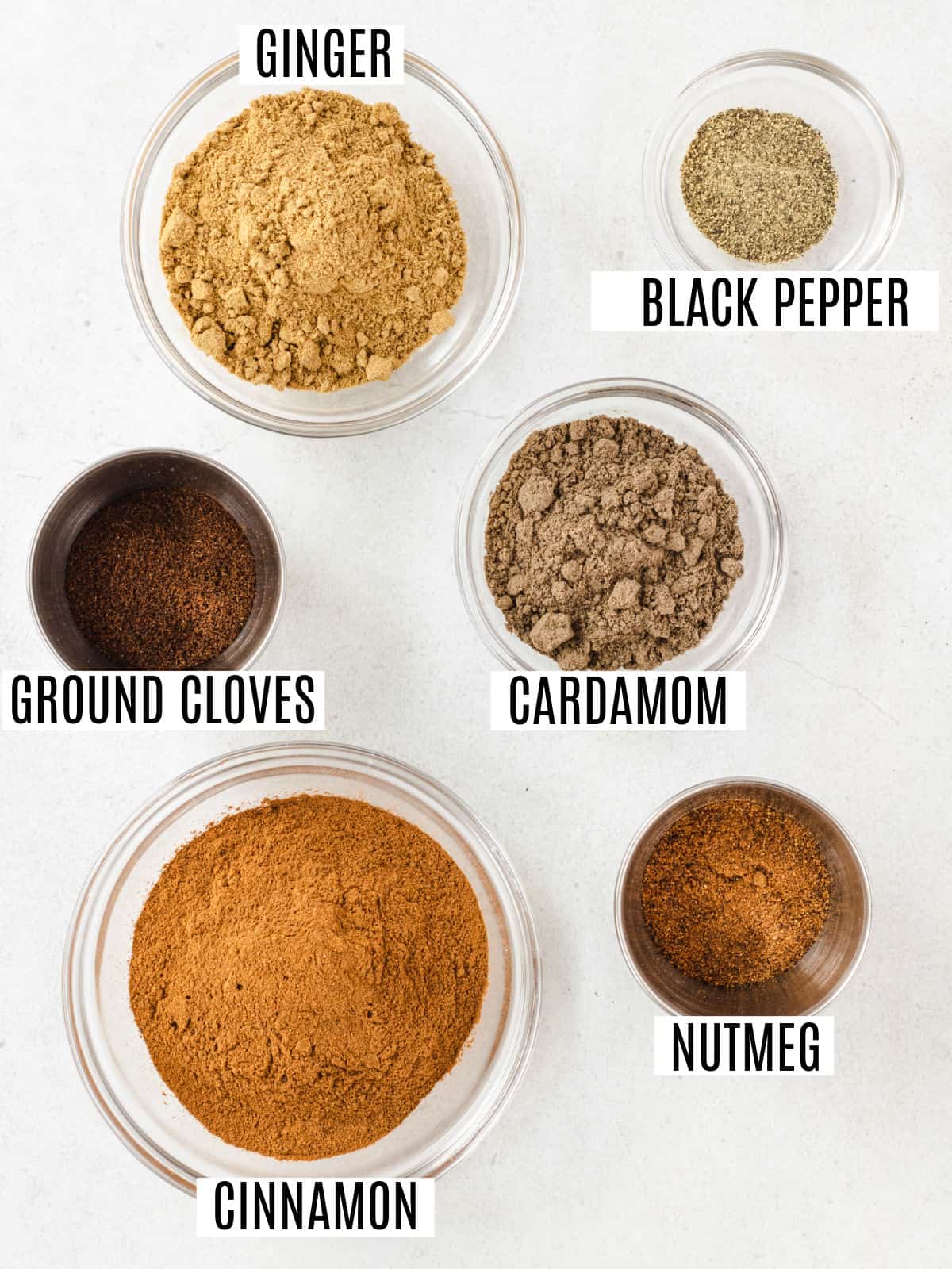 Six ingredients for homemade chai spice mix in bowls.