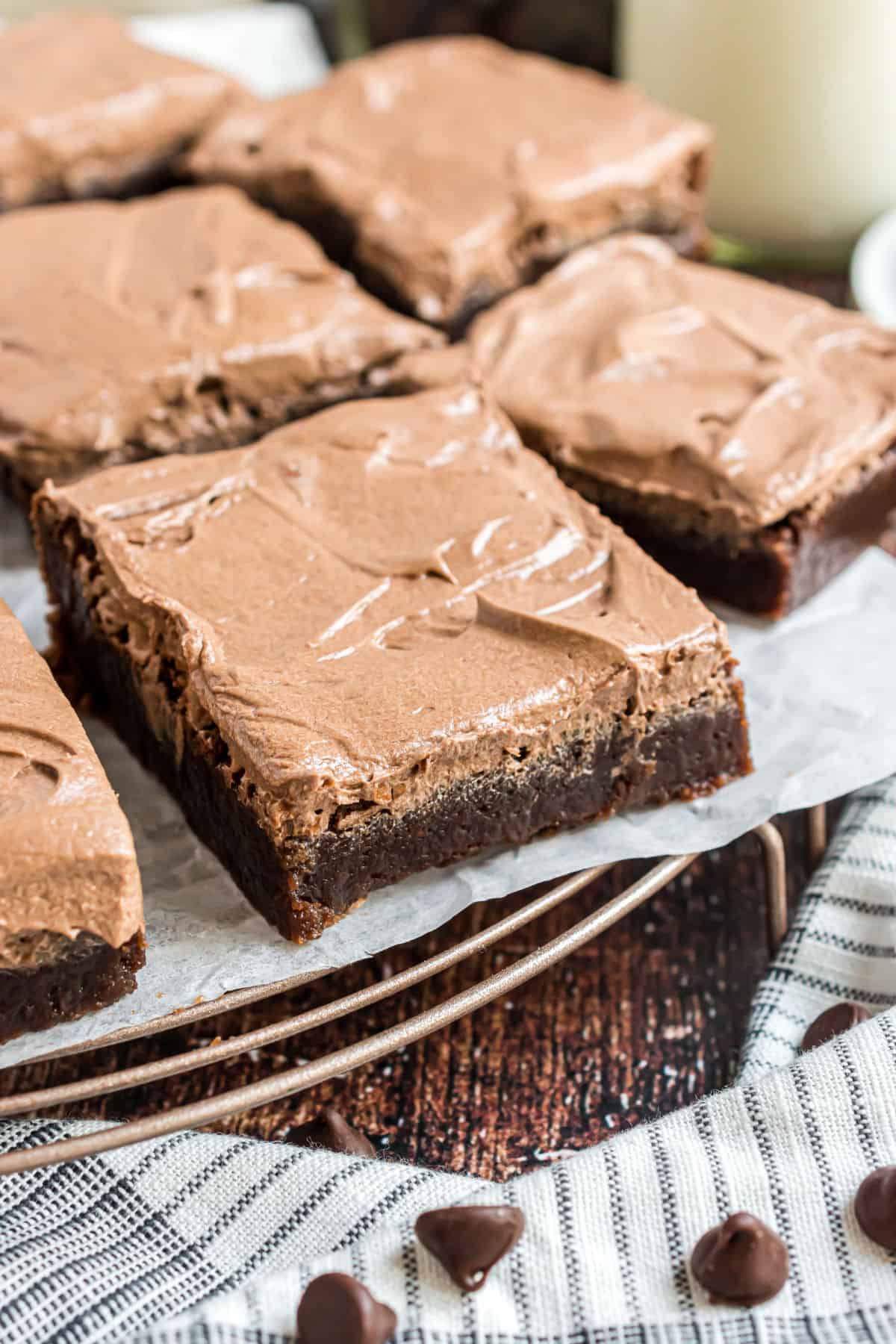 Chocolate frosted brownies on a wire cooling rack with parchment paper.