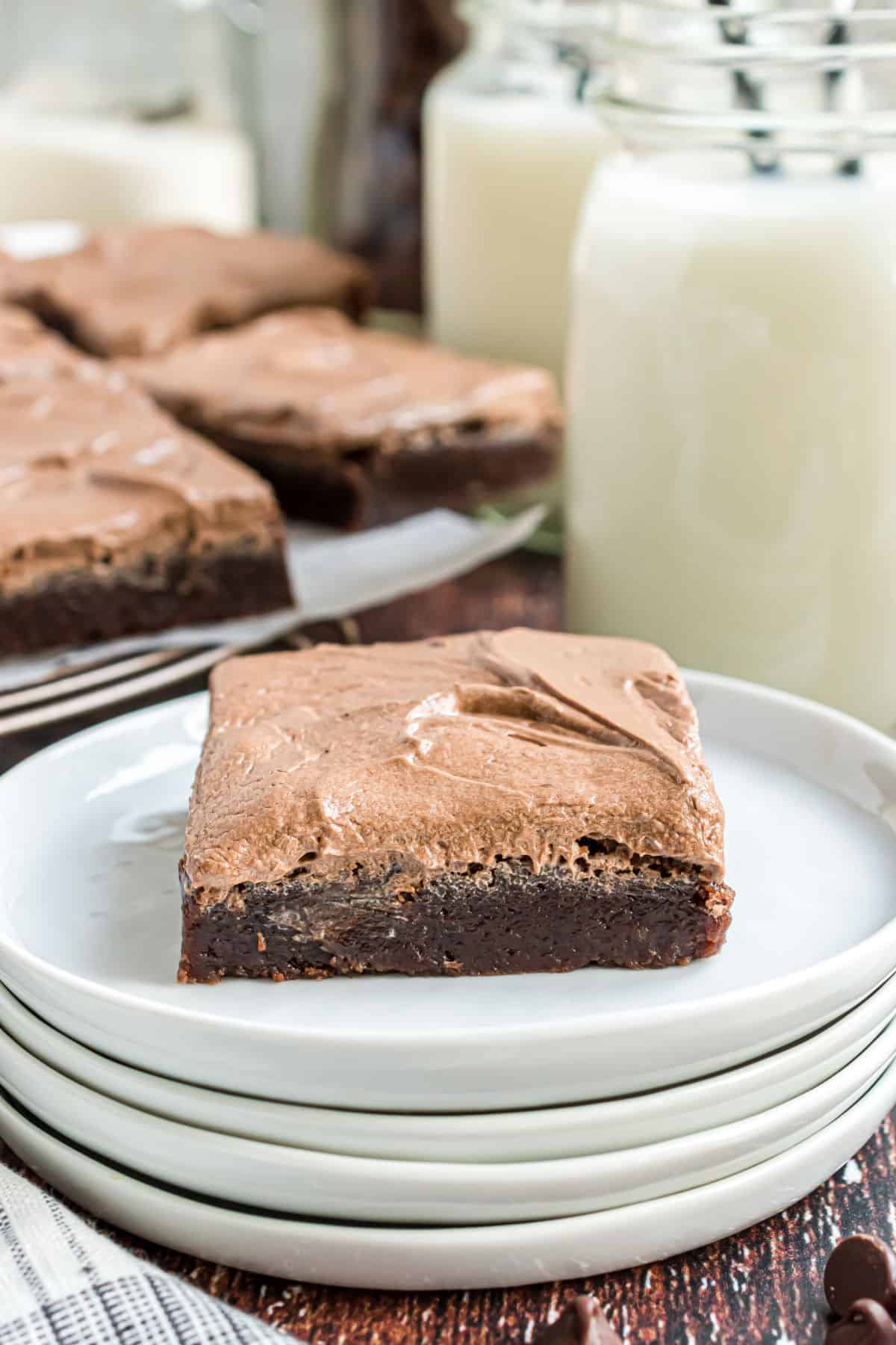 Chocolate brownie with frosting served on a stack of white dessert plates.