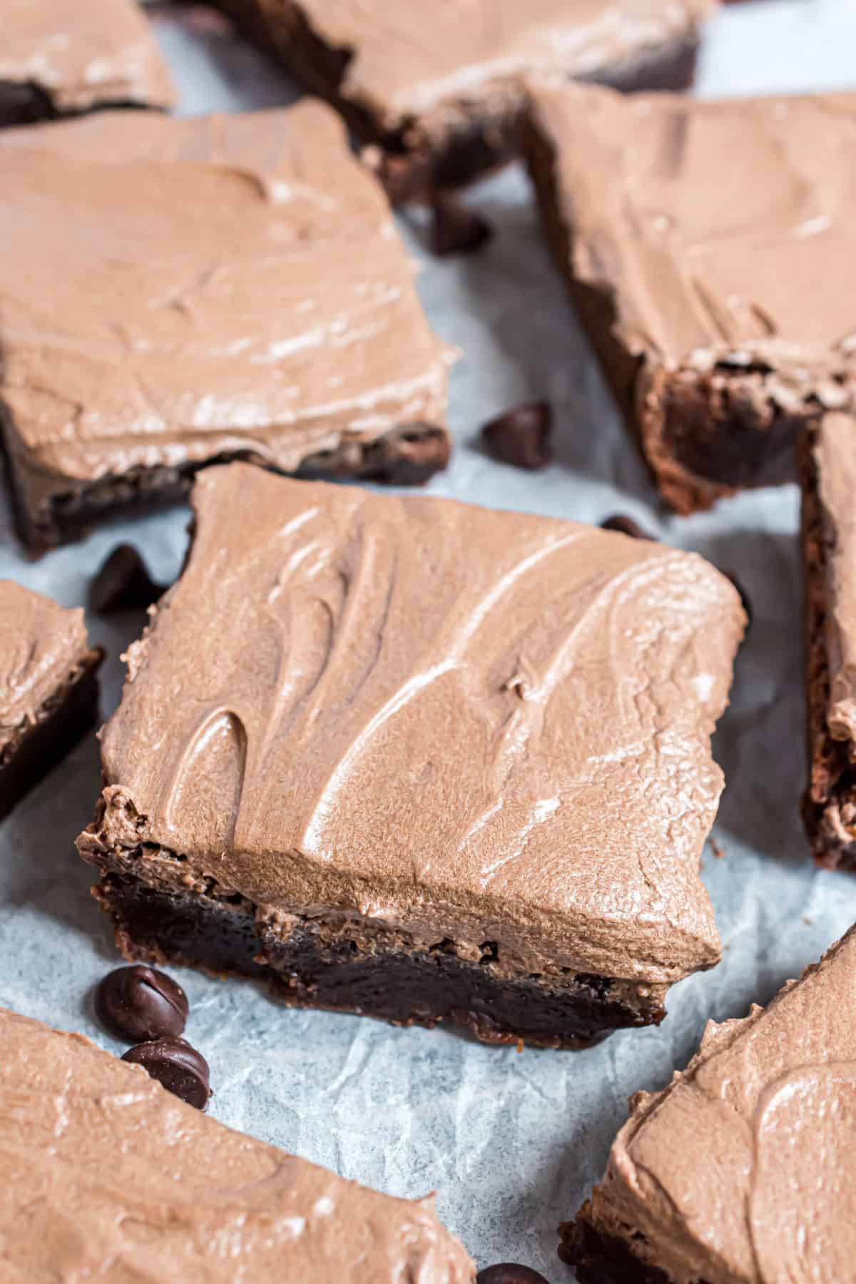 Frosted brownies cut into squares on parchment paper.