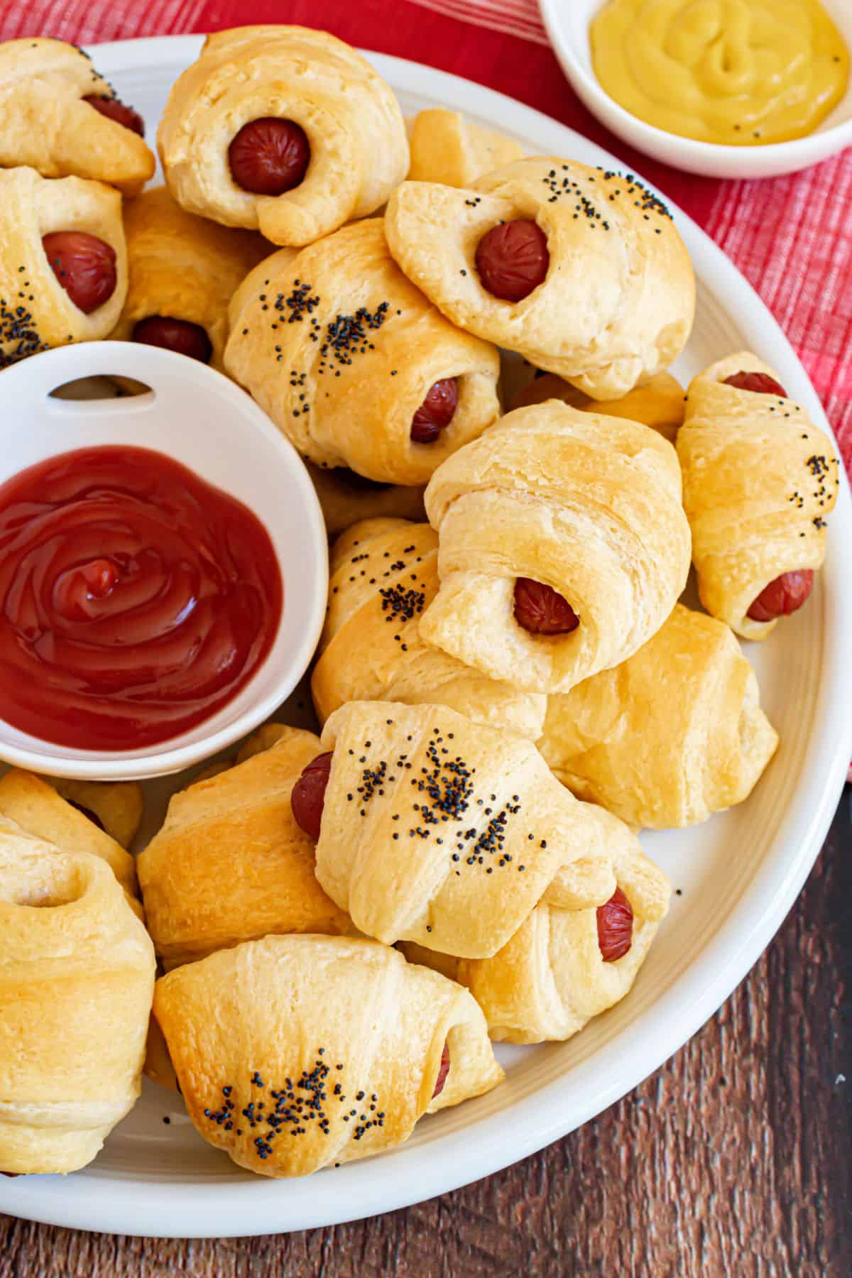 Pigs in a blanket on serving tray with dipping bowls of ketchup and mustard.