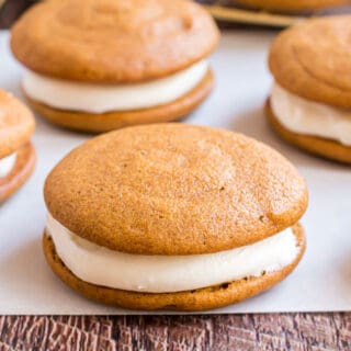 Pumpkin whoopie pie with cream cheese filling on parchment paper.