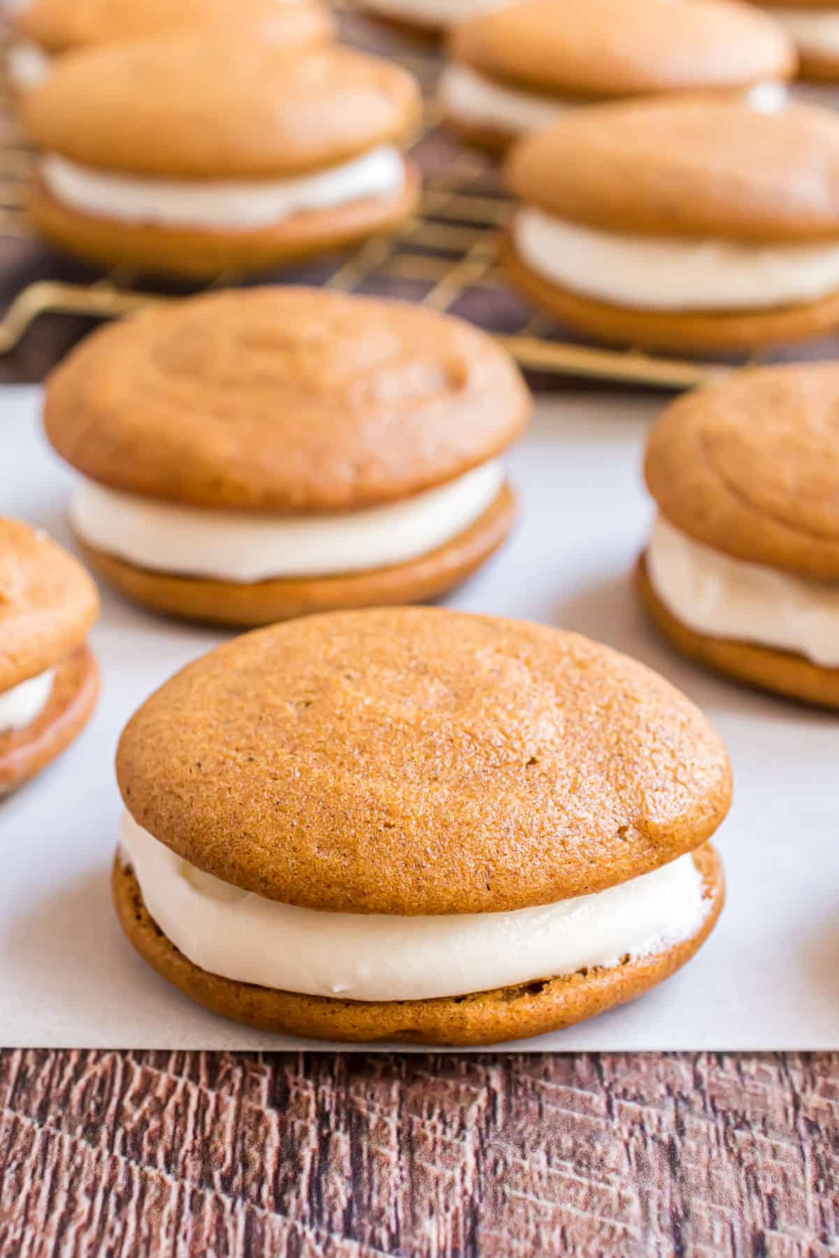 Pumpkin whoopie pies with cream cheese filling on a piece of parchment paper.