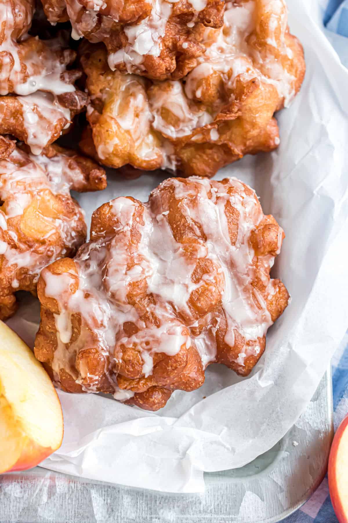 Glazed apple fritters in a parchment paper lined bowl for serving.