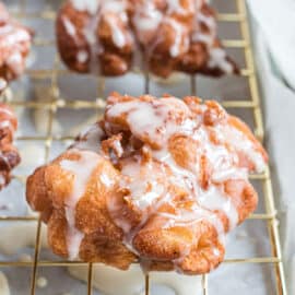 Apple fritter on wire rack with vanilla glaze dripping off.