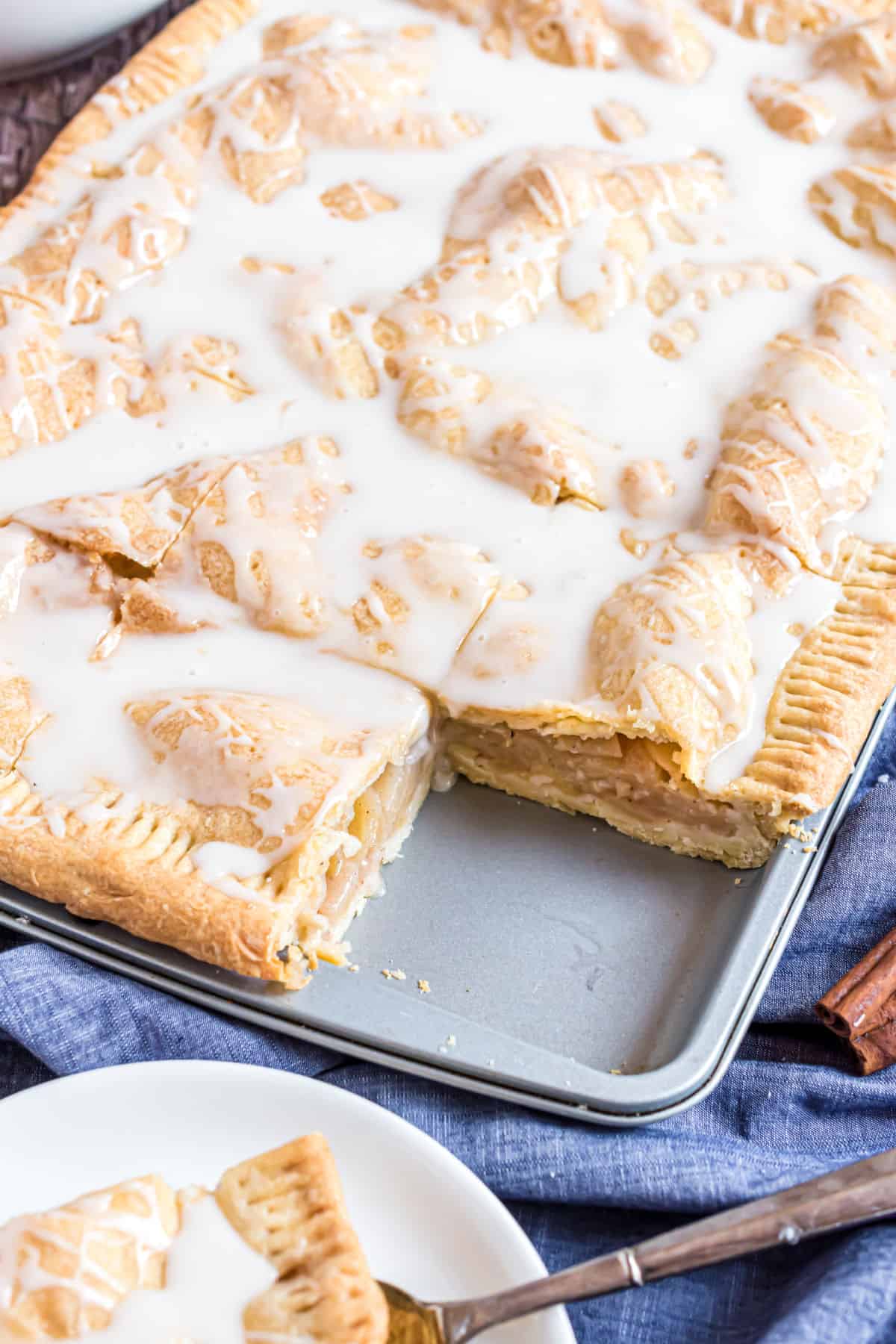 Apple slab pie topped with vanilla icing and one slice removed.