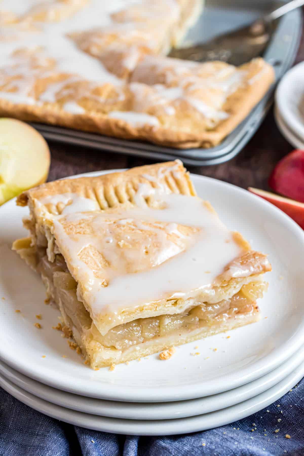 Slice of apple slab pie on a stack of white plates.