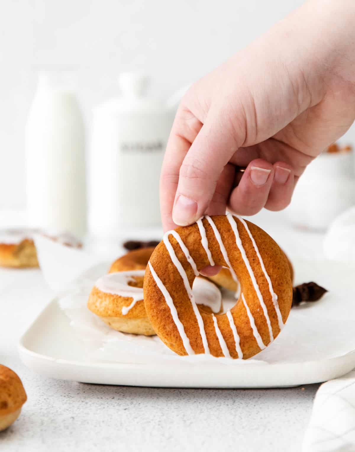 Chai donut with vanilla icing drizzled and a hand picking it up.