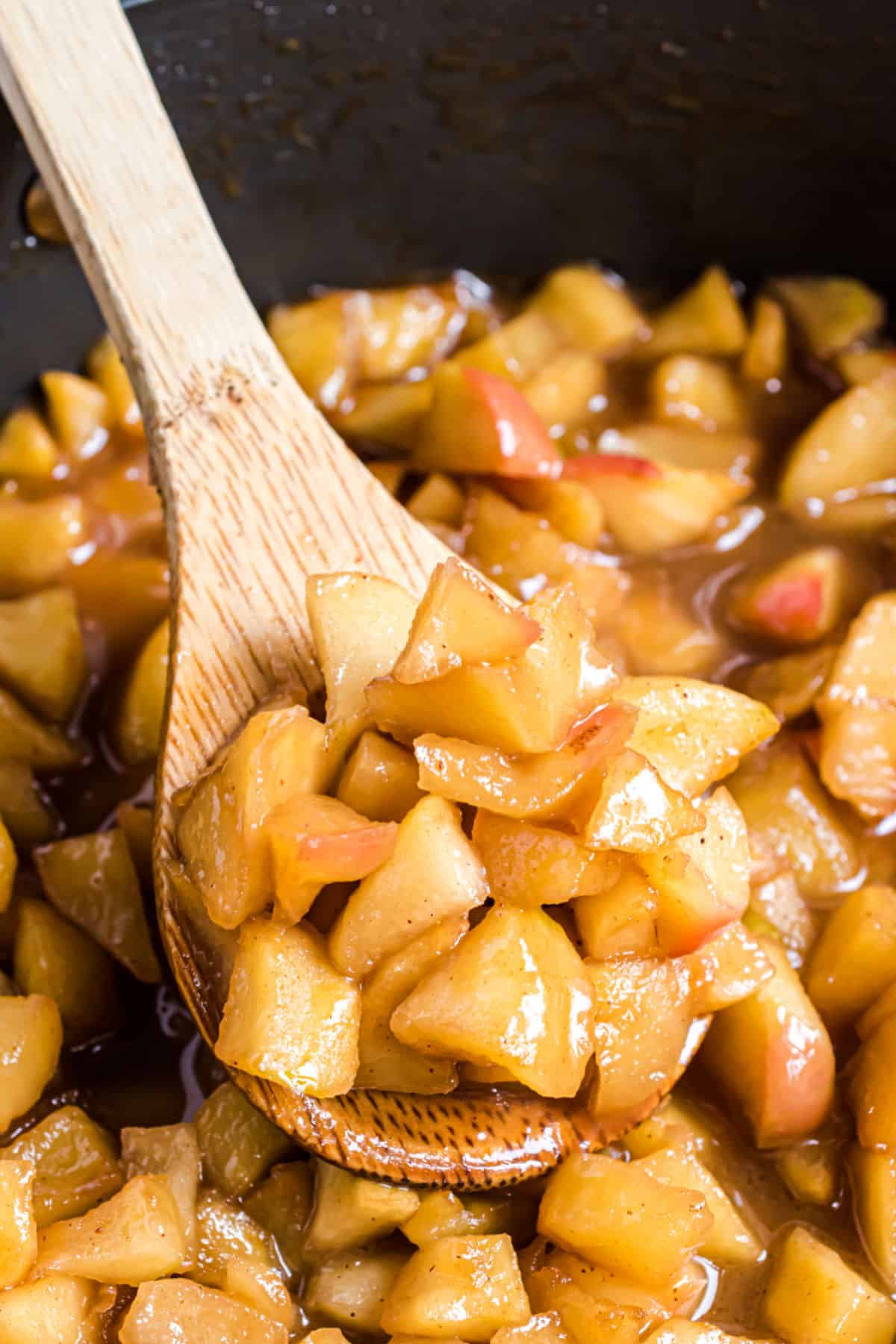 Cinnamon fried apples in skillet with wooden spoon.