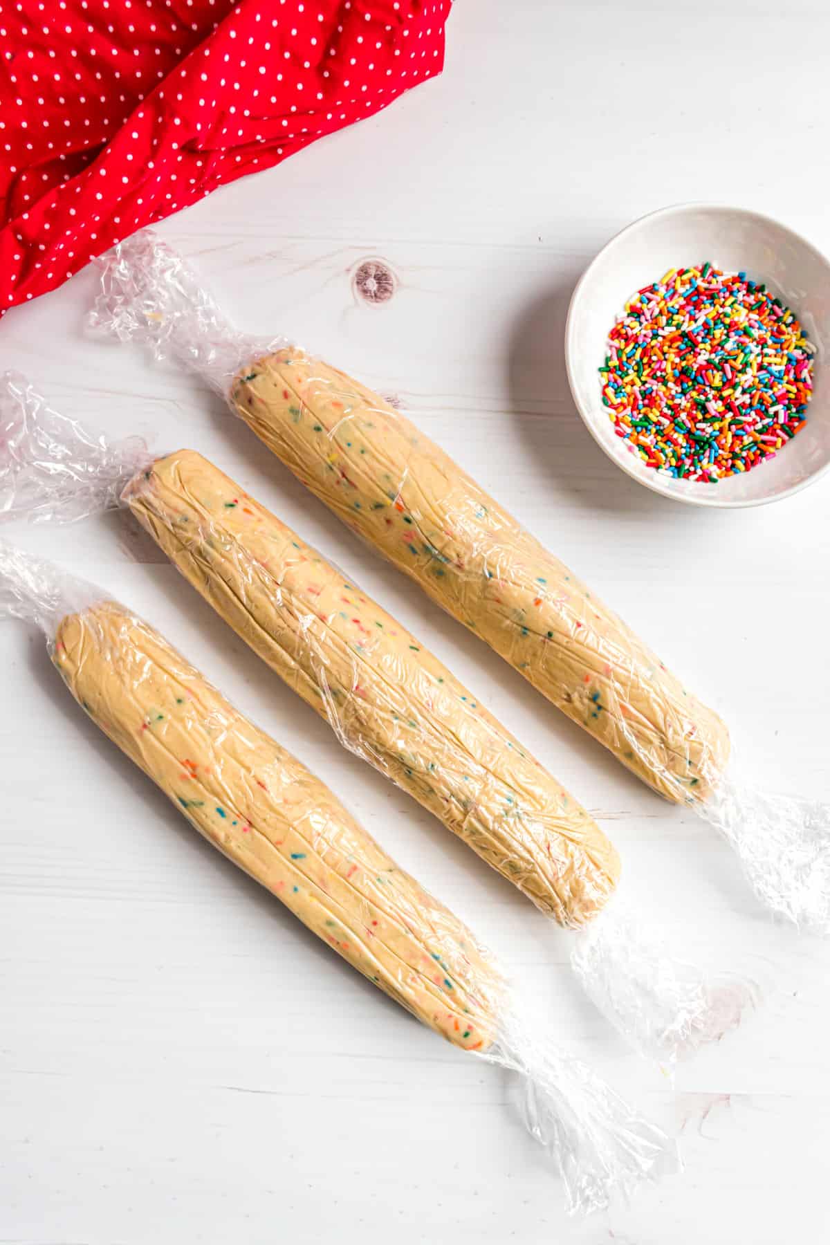 Three logs of icebox cookie dough wrapped in plastic wrap.