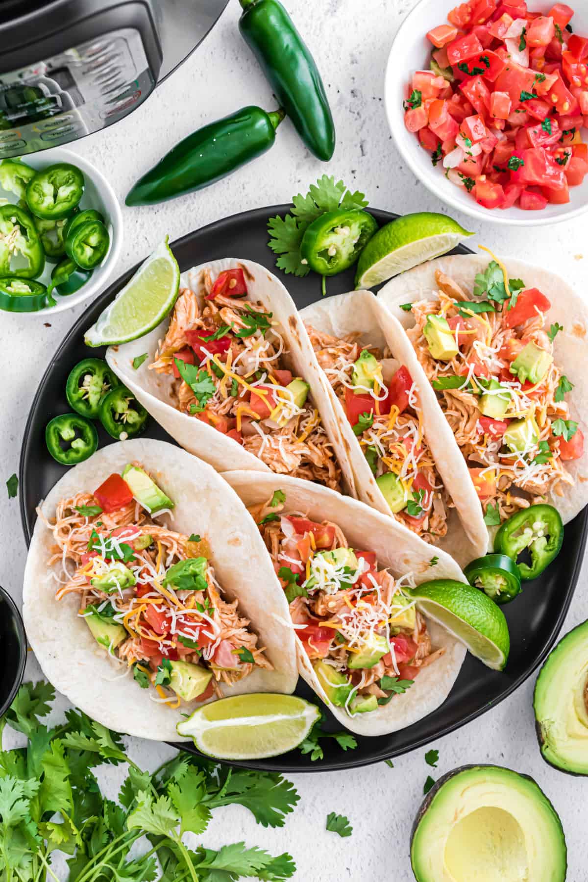 Black serving plate with chicken tacos and fixings.