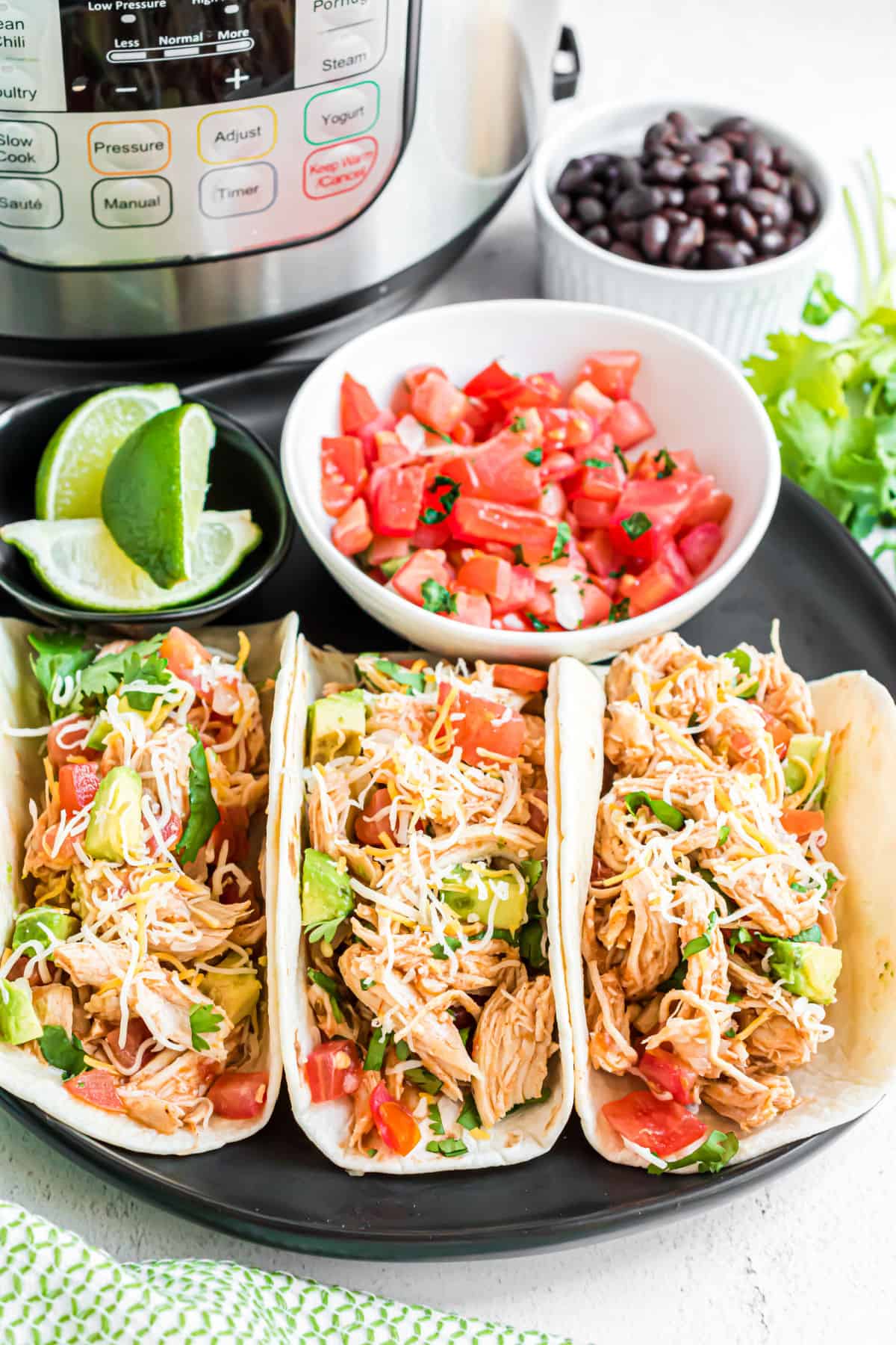 Three chicken tacos with all the fixings and instant pot in background.