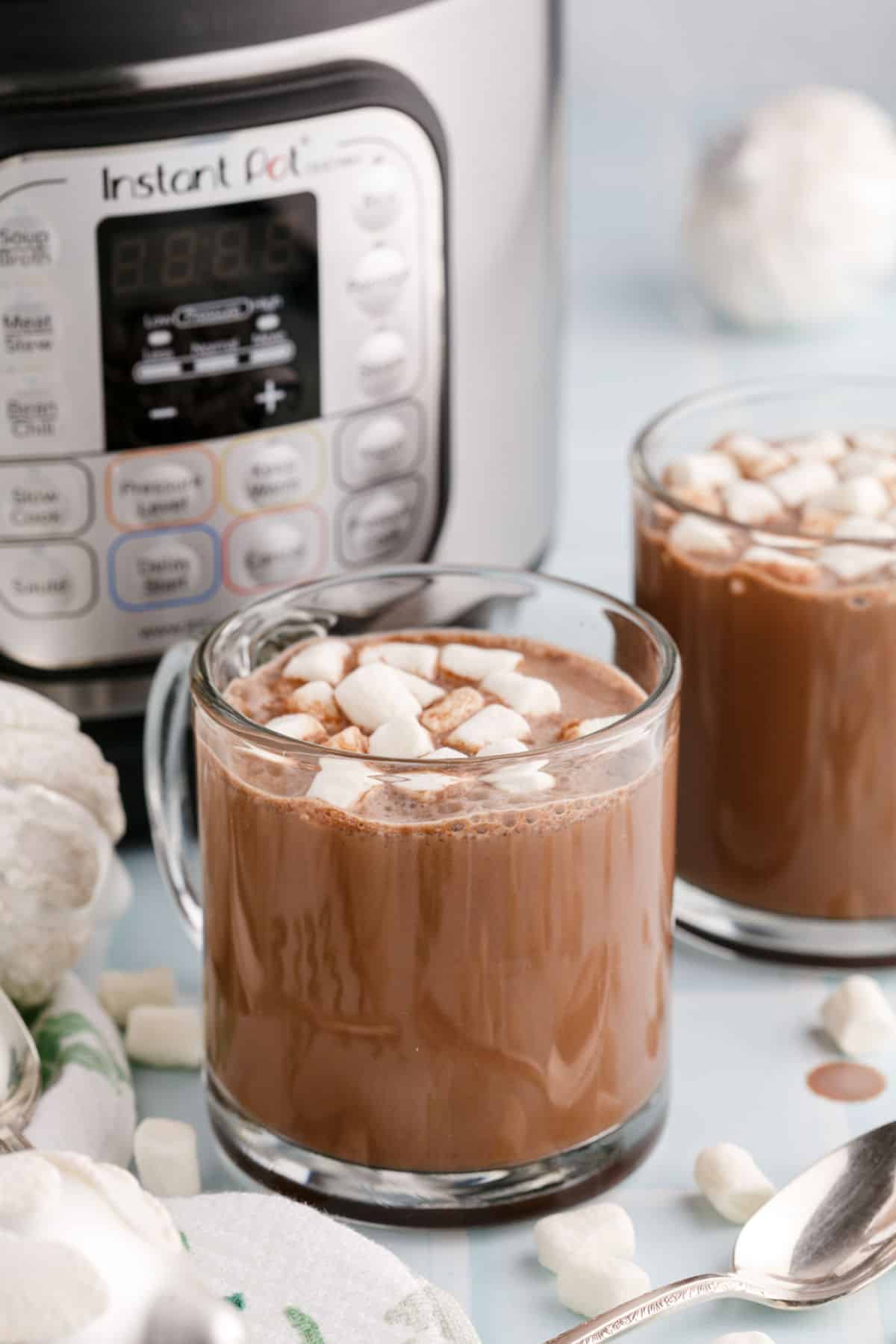 Two clear glass mugs of hot chocolate and marshmallows with Instant Pot in background.