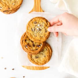 Stack of three andes mint cookies on parchment paper lined cutting board.