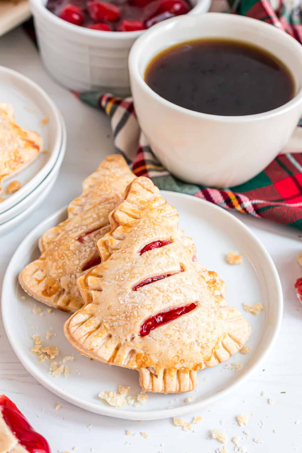 Two cherry hand pies on a white plate with a cup of coffee.