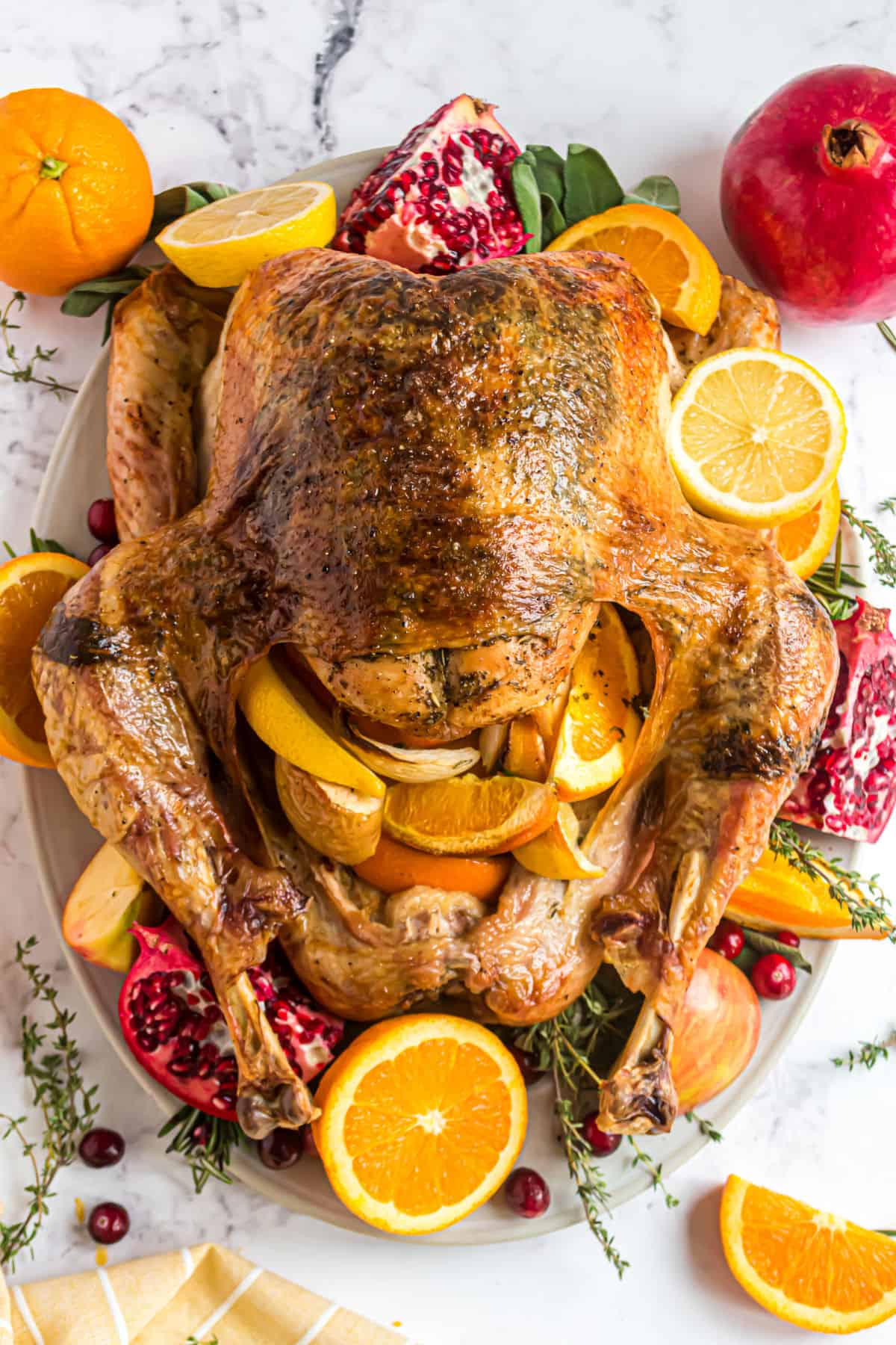 Oven roasted turkey on a platter with oranges, pomegranates, and herbs.