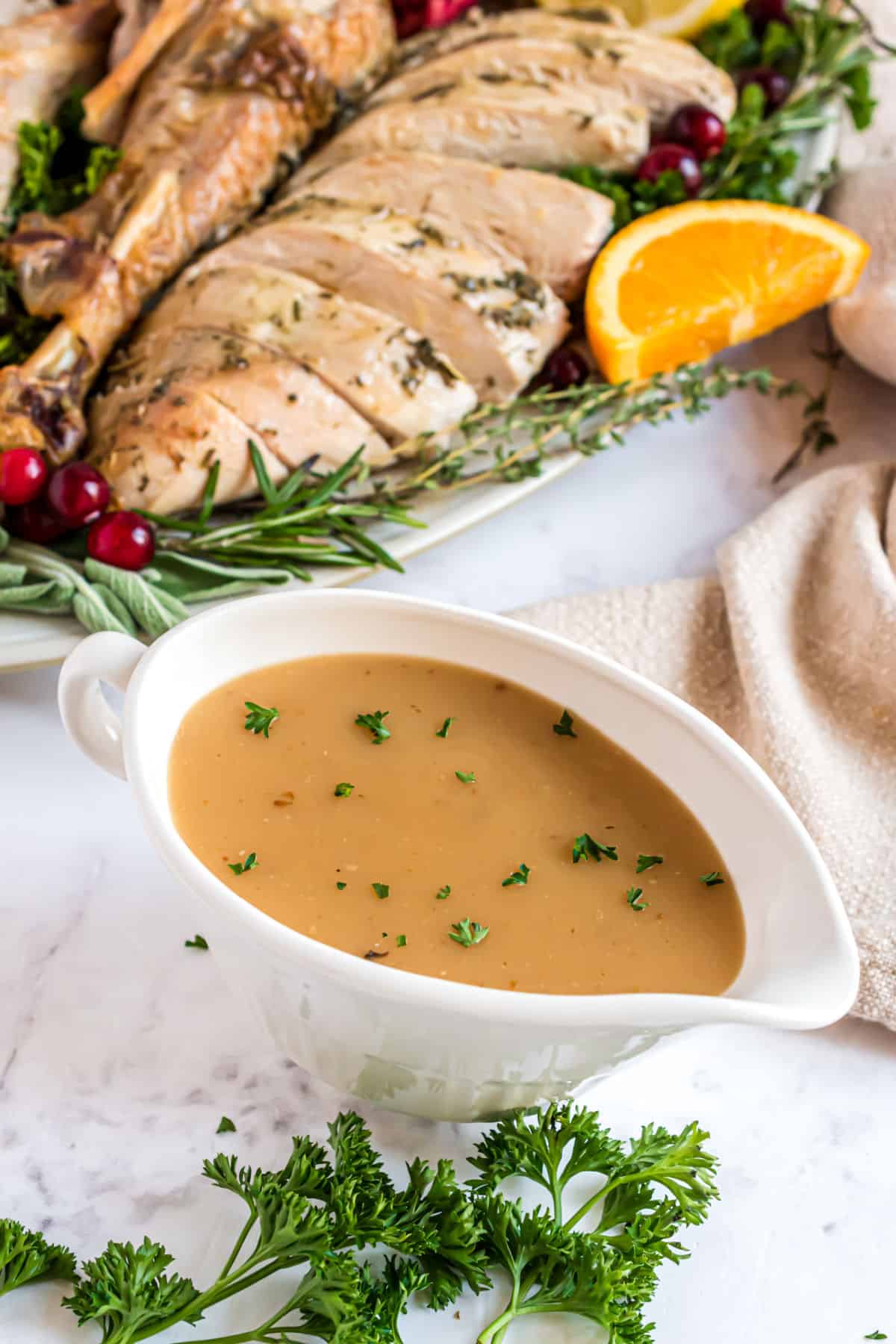 Turkey gravy in white gravy boat with carved turkey in background.