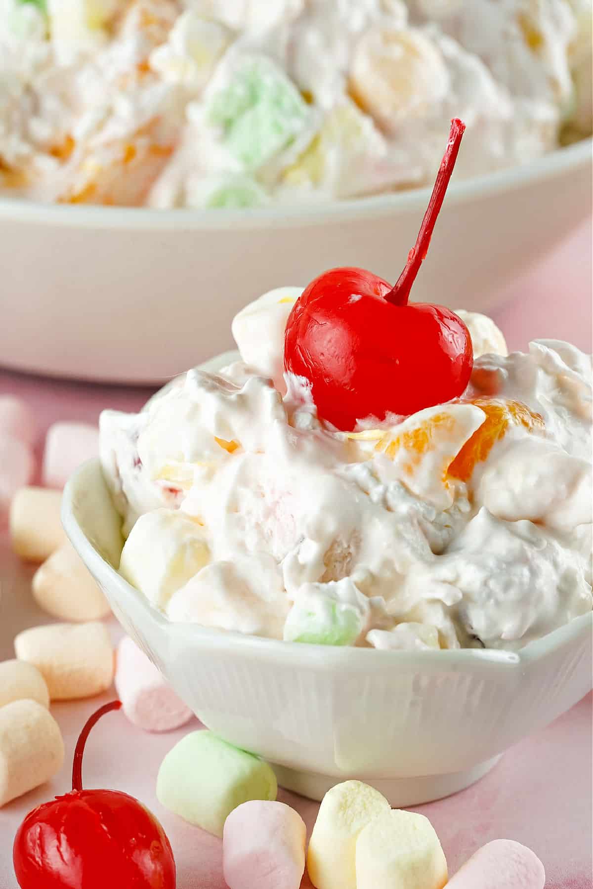 Ambrosia salad in a bowl topped with maraschino cherry.