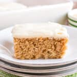 Big slice of applesauce cake on a white plate and topped with cream cheese icing.