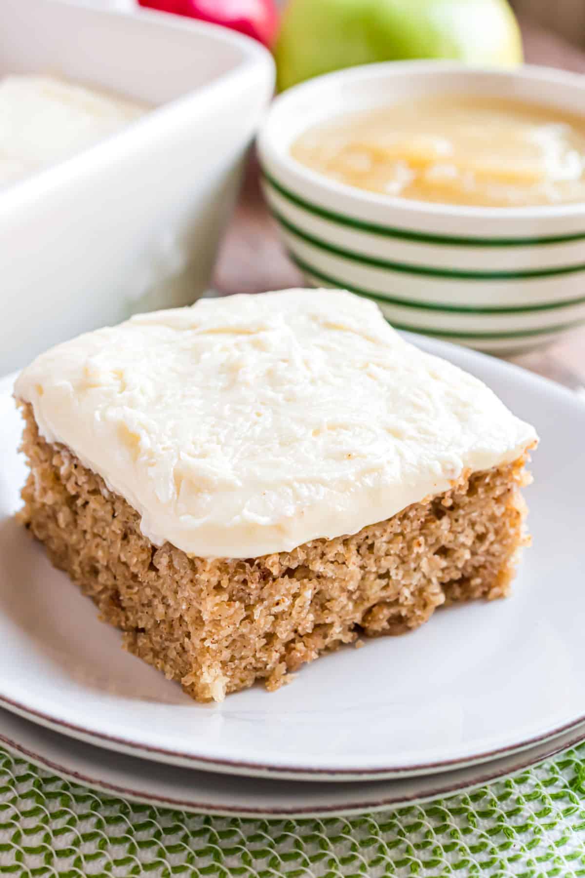Slice of applesauce cake with cream cheese frosting on a white dessert plate.