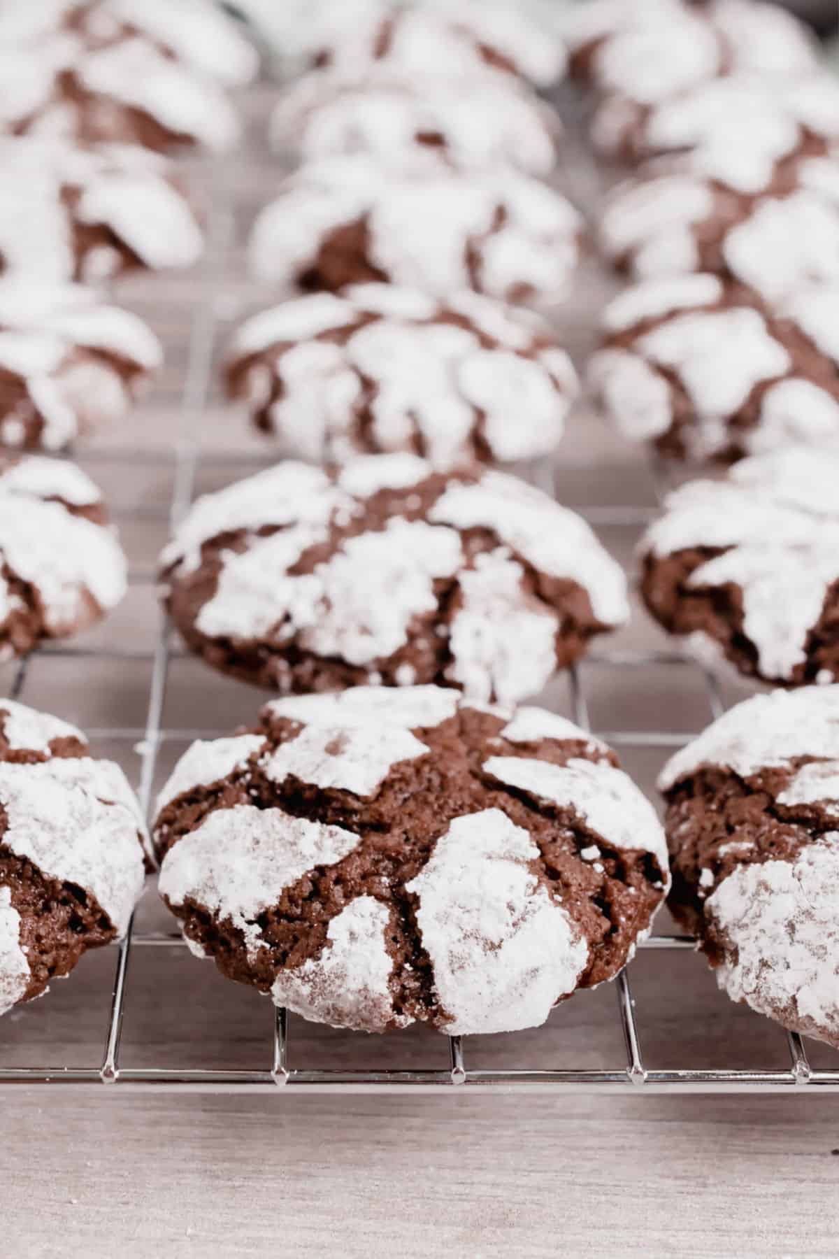 Chocolate crinkle cookies with powdered sugar on metal cooling rack.