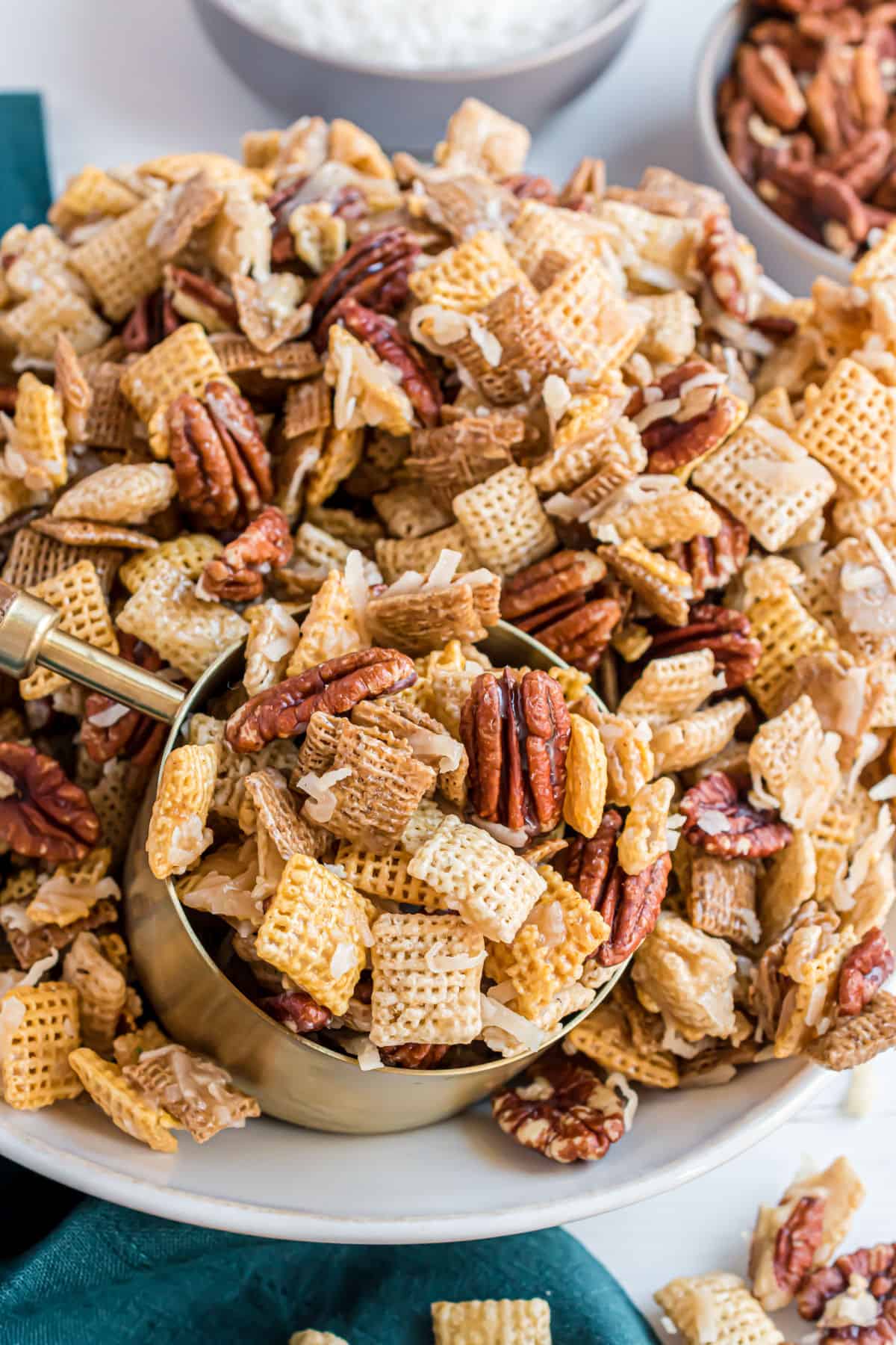Sweet holiday chex mix in a large bowl with a measure cup to scoop and serve.