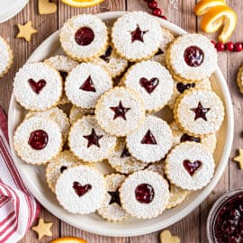 Large white serving platter with linzer cookies stacked on top.