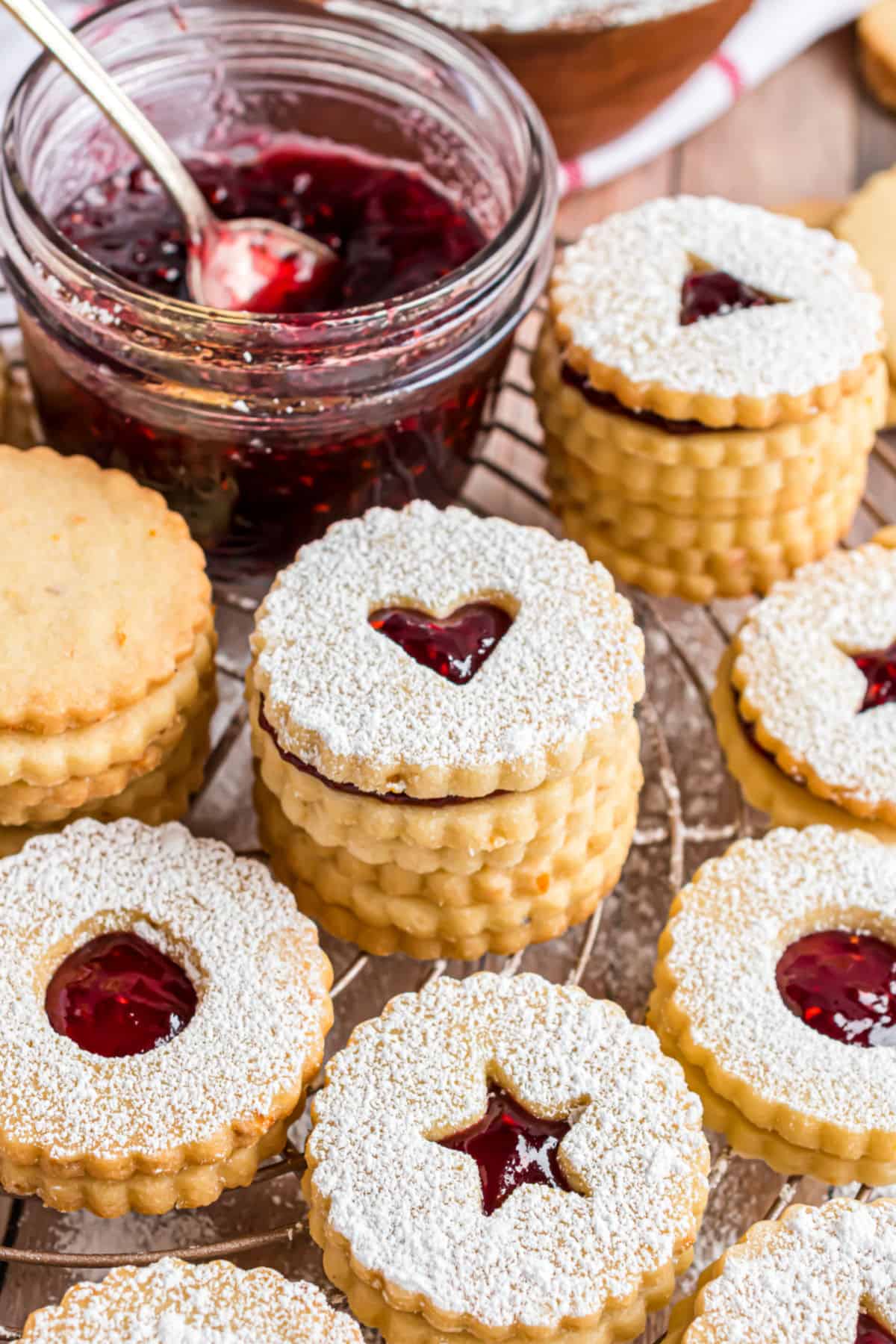 Linzer cookies stacked on a wire rack with a jar of jam in background.
